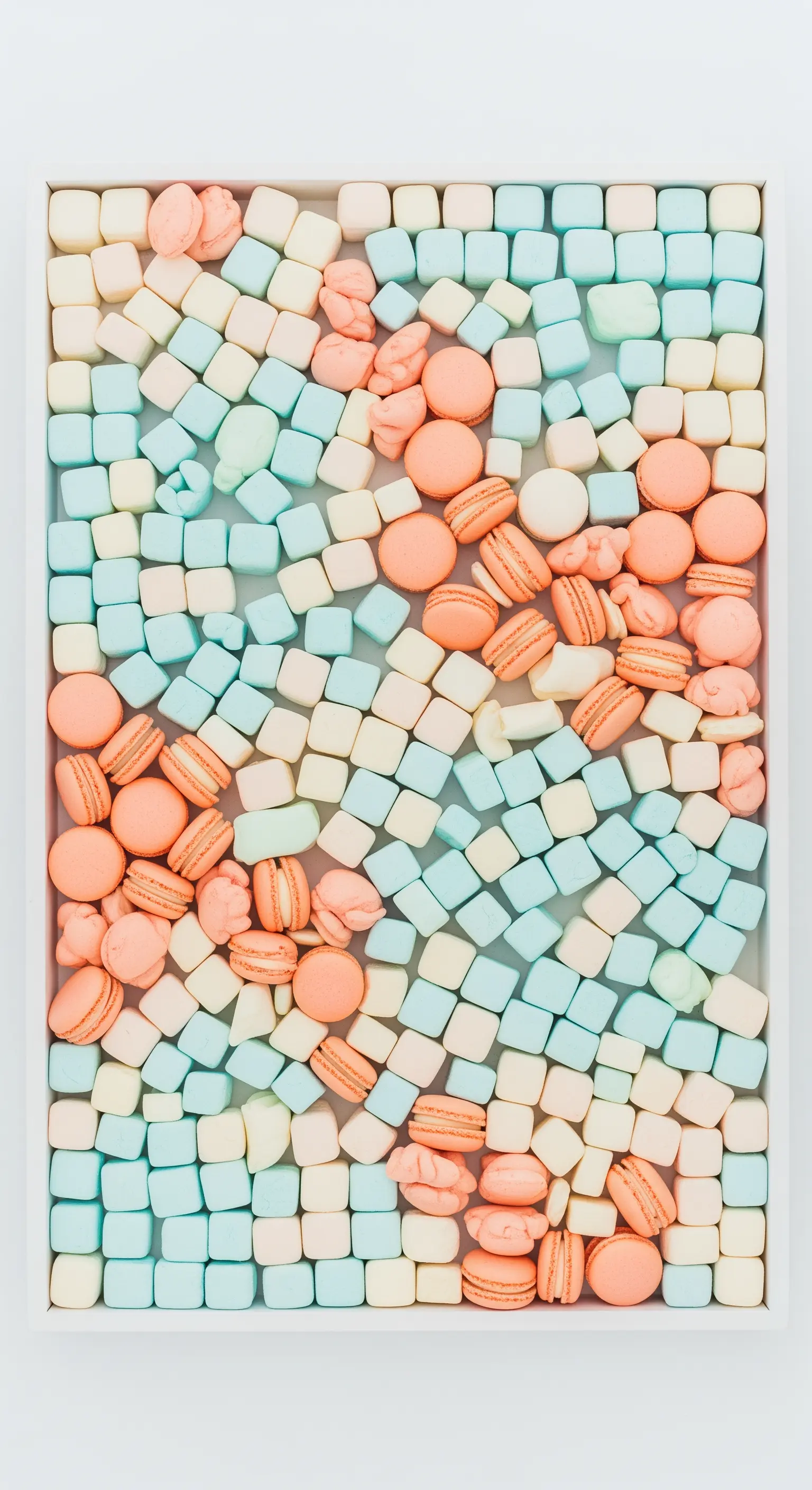 Composizione a mosaico con marshmallow e macarons color pastello in un vassoio bianco.