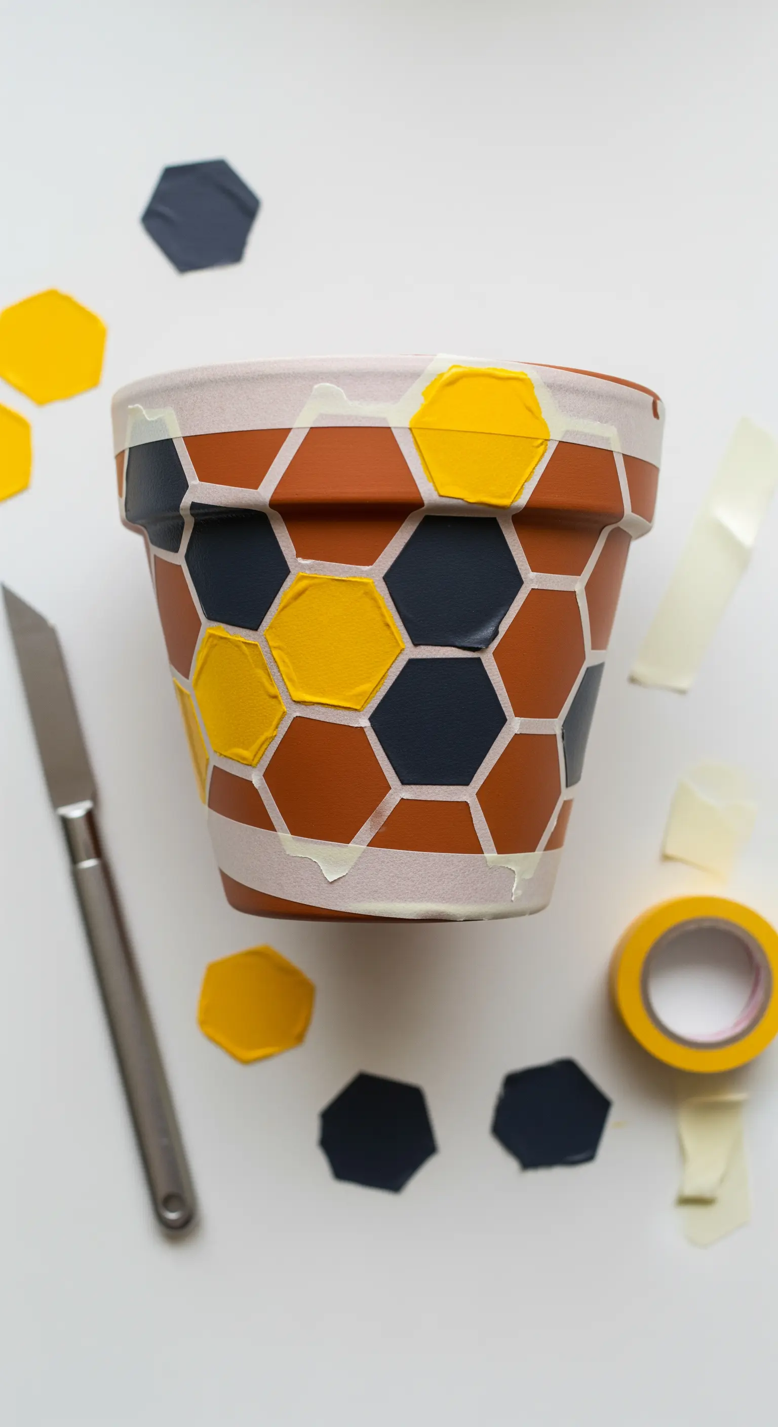 Vaso in terracotta in fase di decorazione con un motivo a esagoni gialli e blu, usando nastro adesivo.