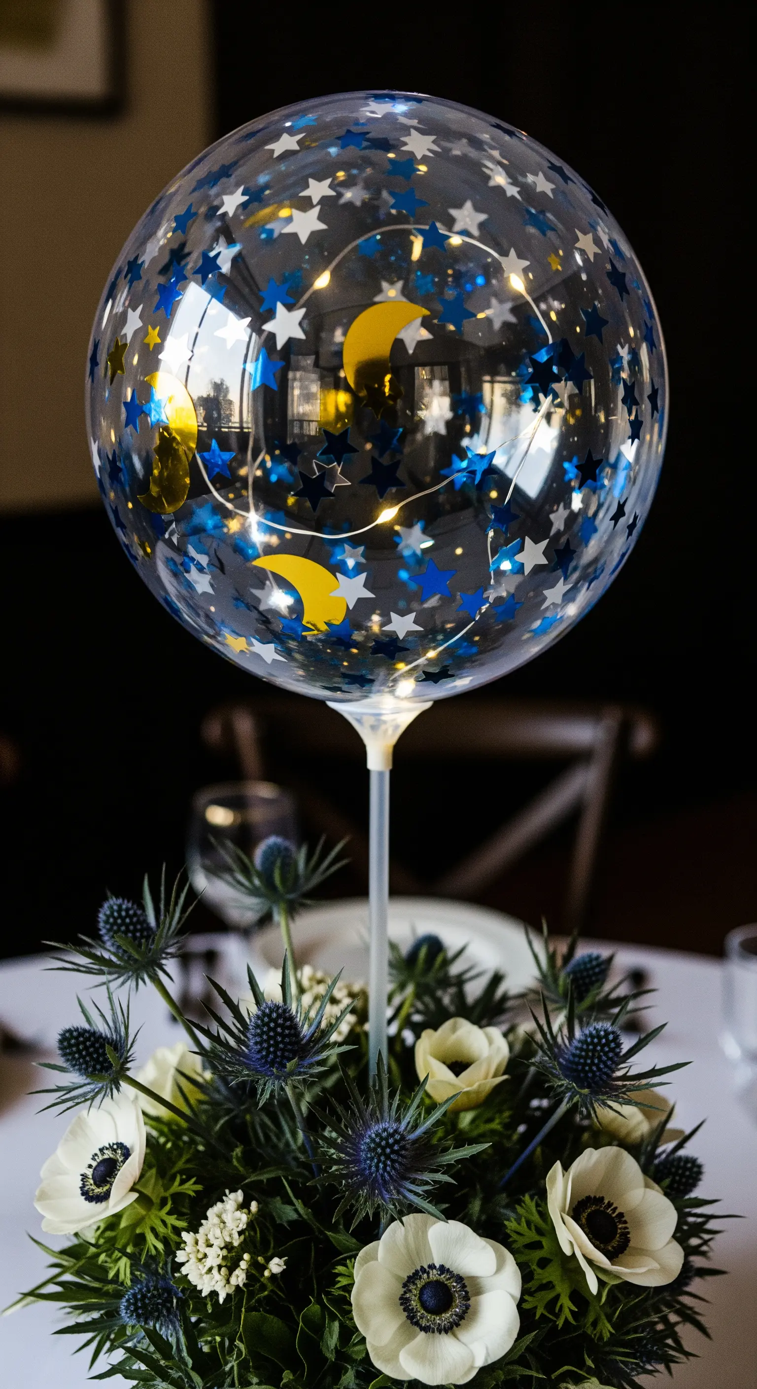 Palloncino con coriandoli a forma di stelle e luna, sopra un bouquet di anemoni e cardi blu.