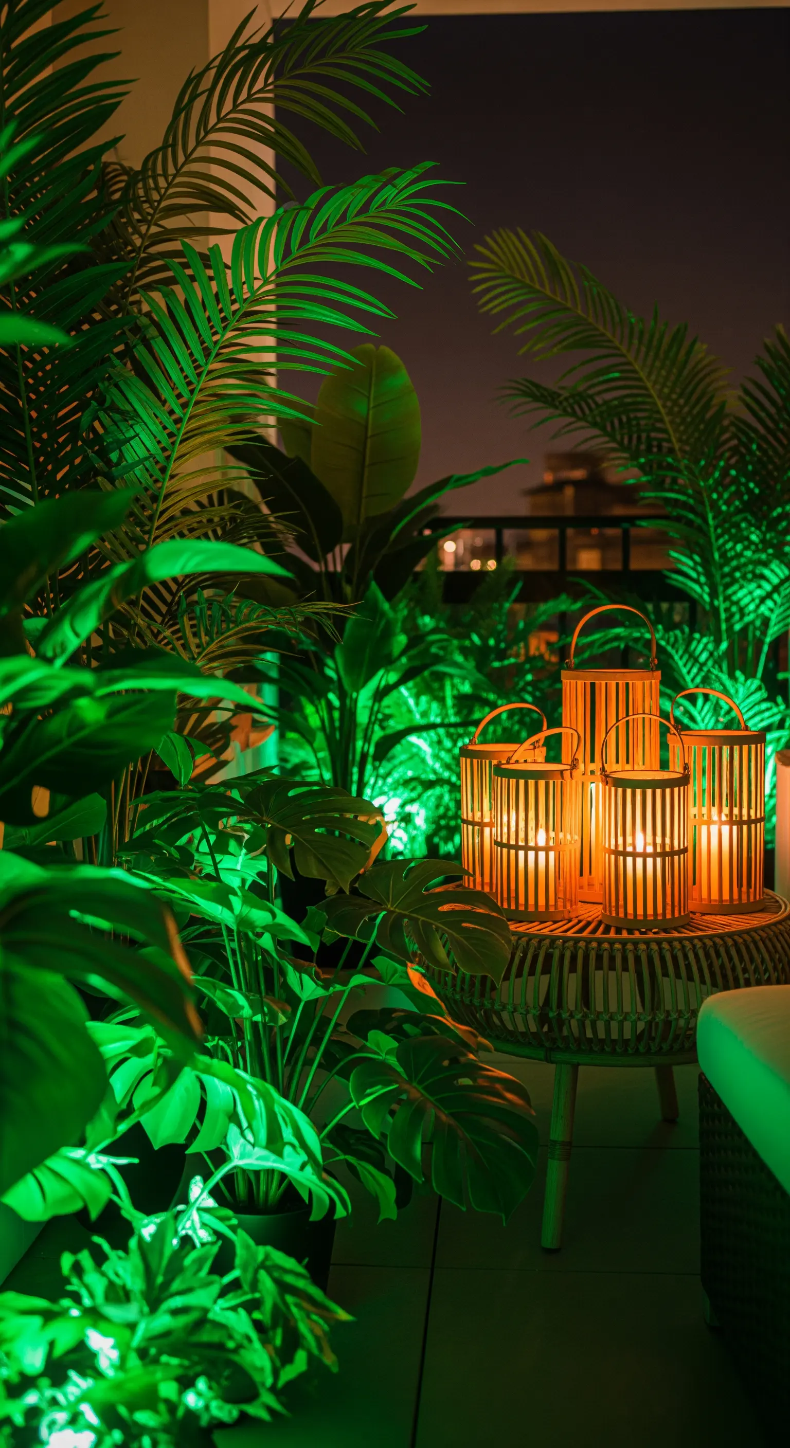 Angolo di un balcone con piante tropicali illuminate da una luce verde e lanterne in bambù con candele