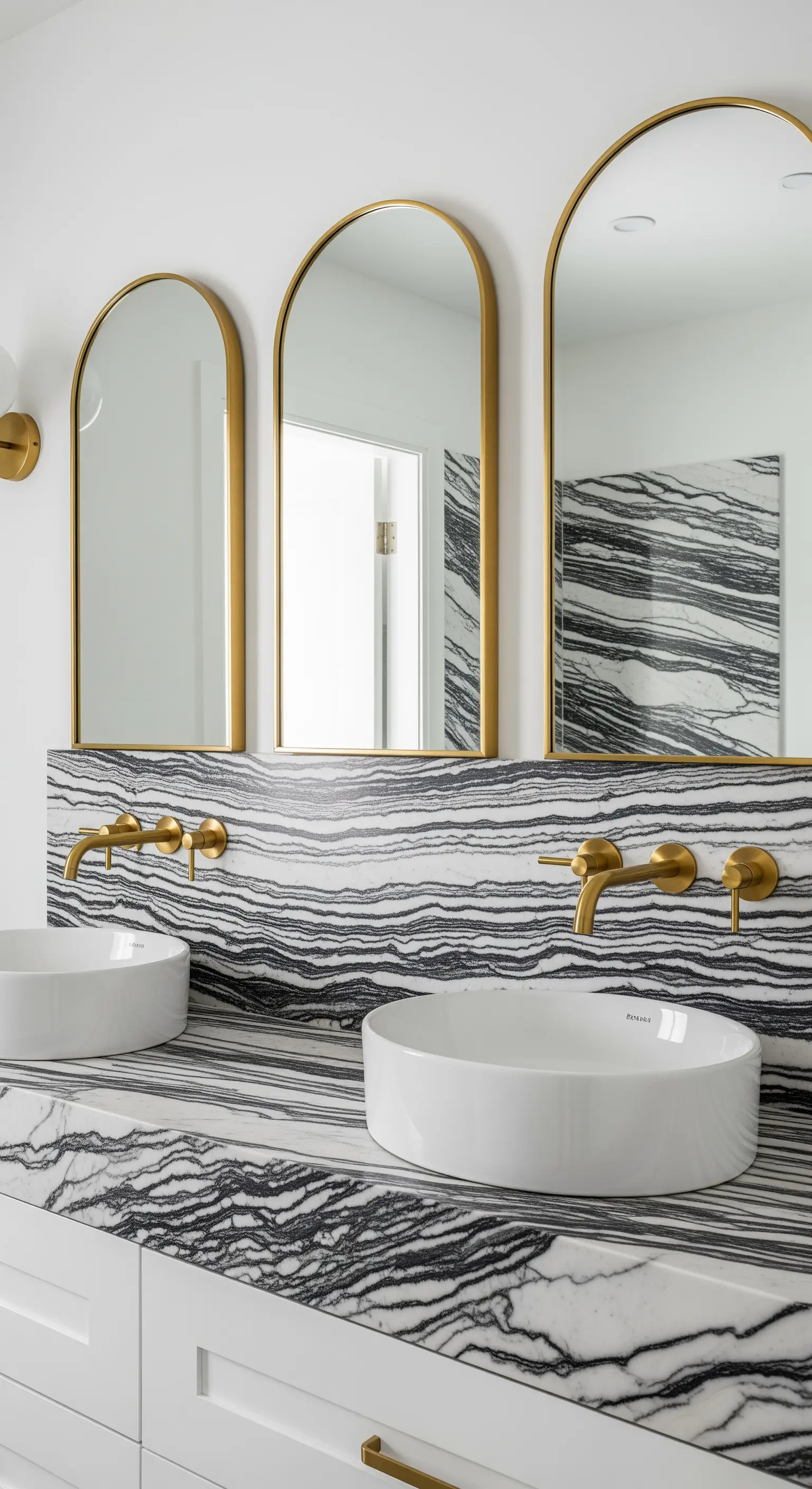 Doppio lavabo con top e paraschizzi in marmo a venature orizzontali e specchi ad arco dorati.