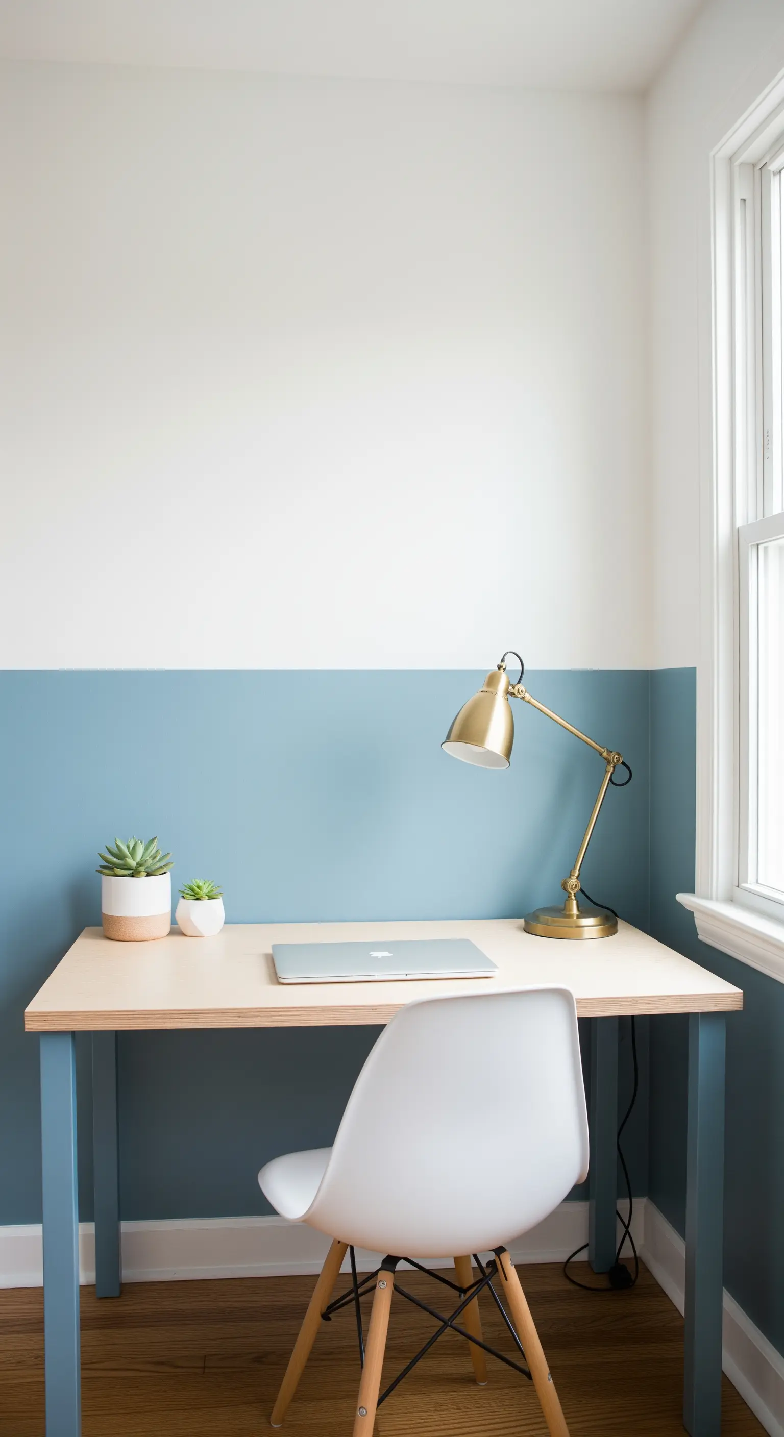 Scrivania in legno chiaro contro una parete dipinta a metà, blu sotto e bianco sopra.