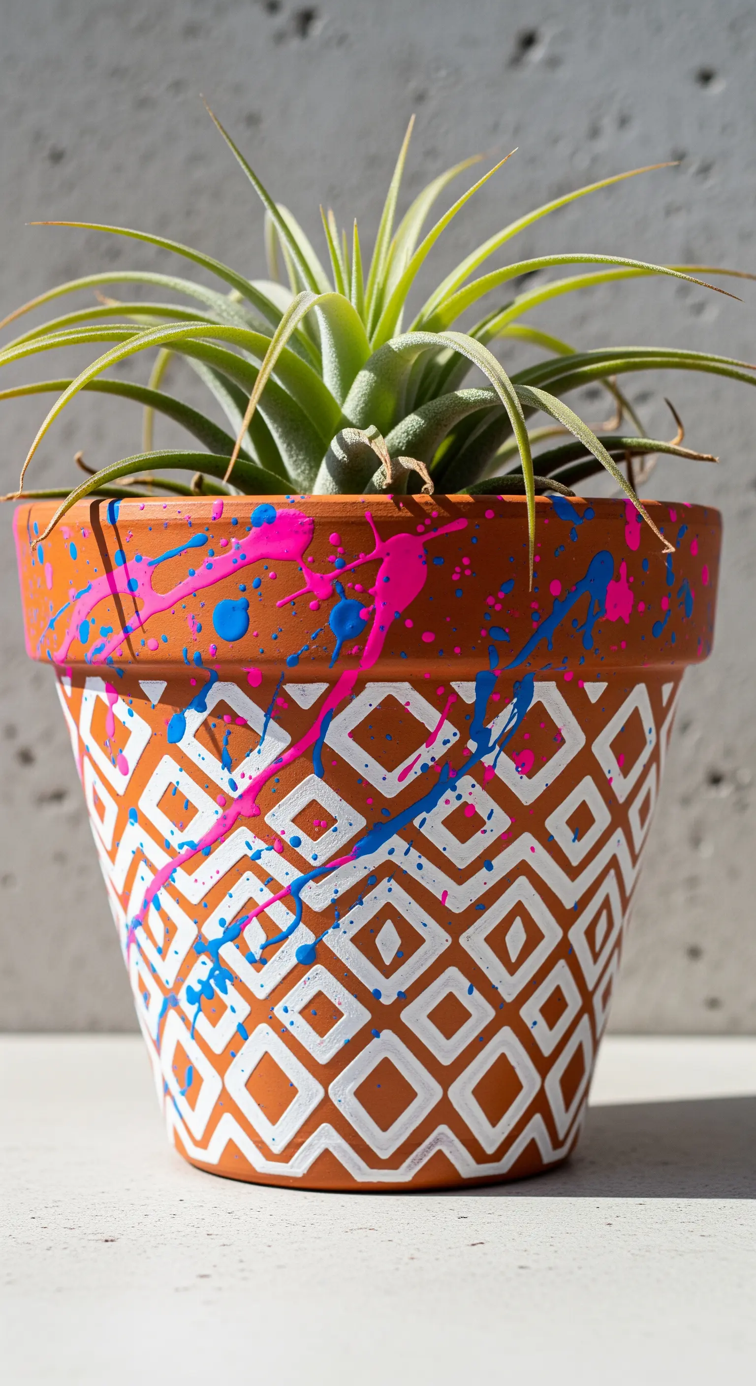 Vaso di terracotta con un motivo a rombi bianchi e schizzi di vernice fucsia e ciano.