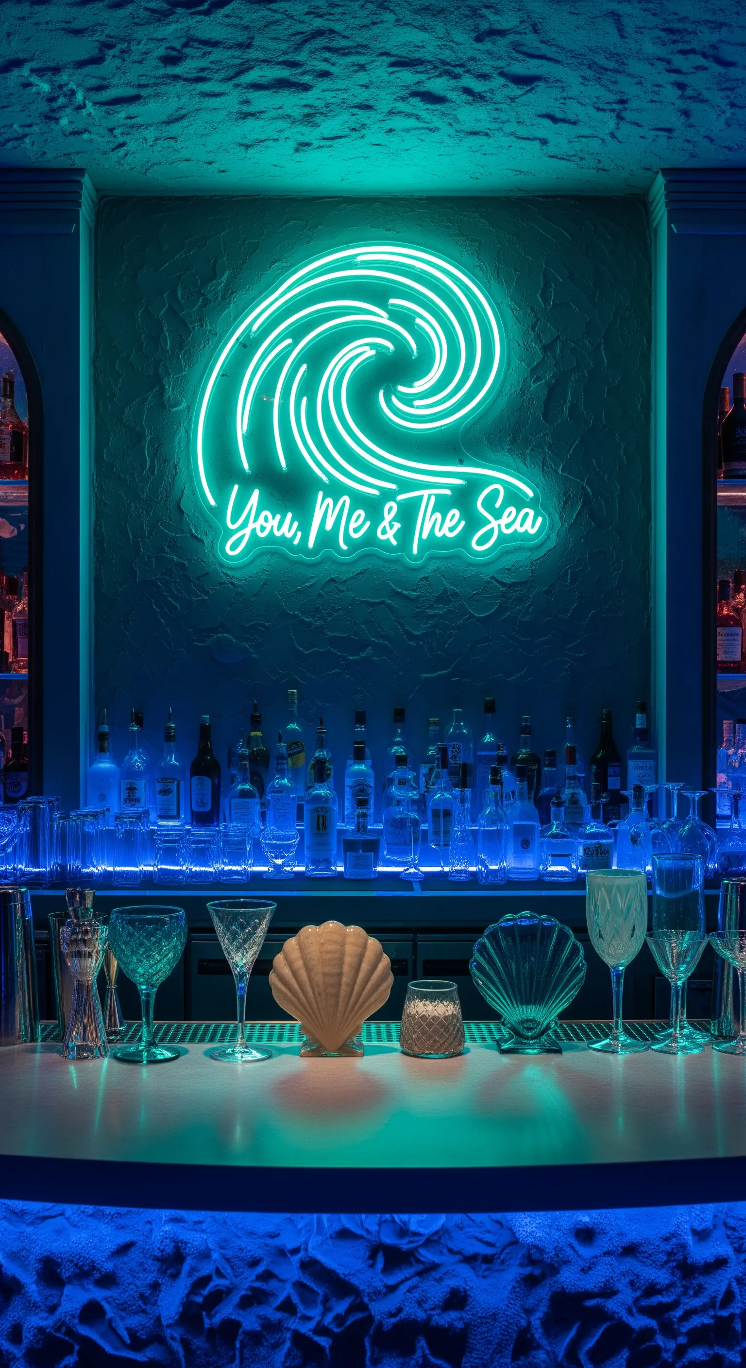 Neon a forma di onda “You, Me & The Sea” su una parete blu texturizzata con conchiglie.