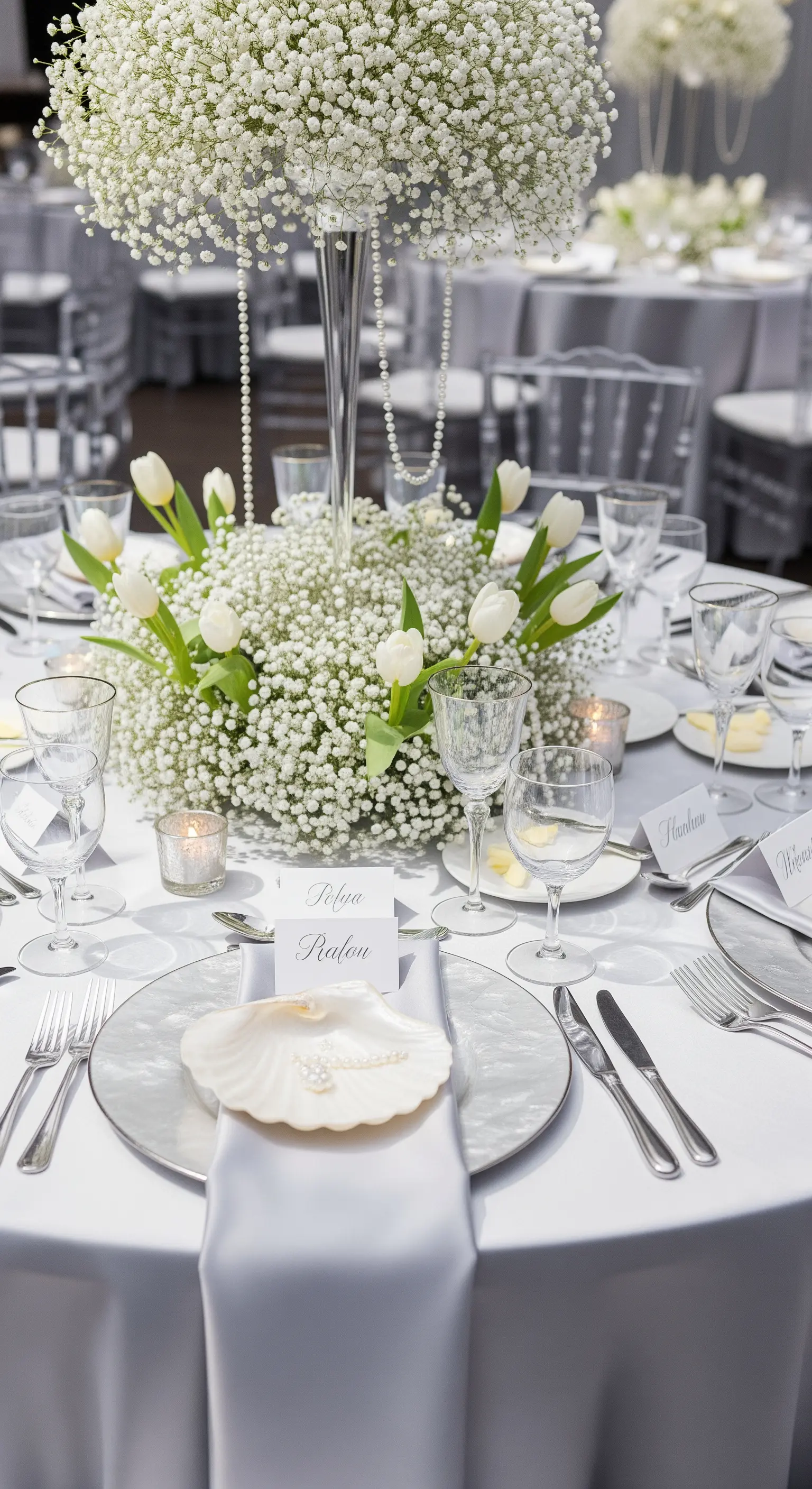 Tavola total white con centrotavola di gypsophila, perle e segnaposto a conchiglia.