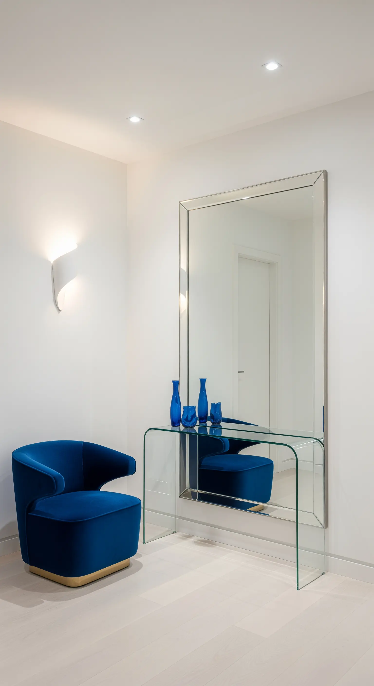 Ingresso minimalista con specchio a tutta altezza, consolle in vetro e poltrona in velluto blu