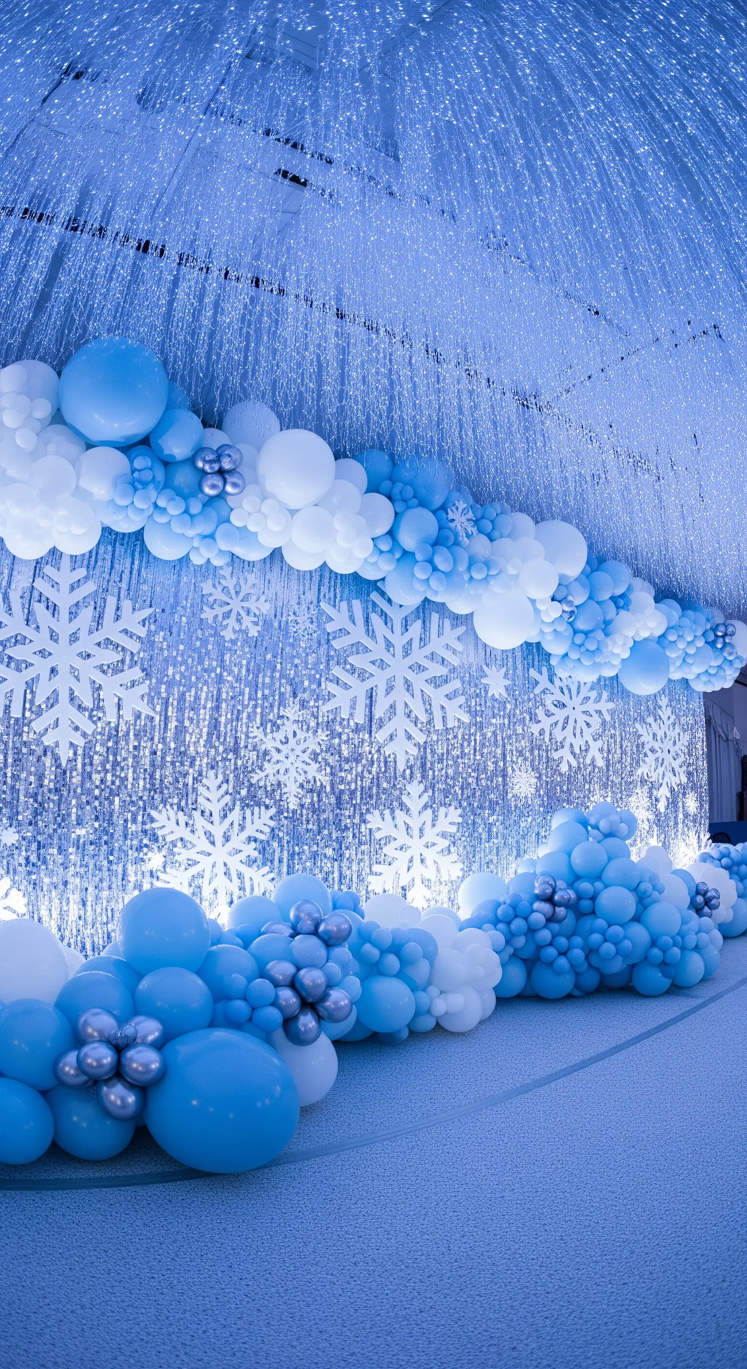Allestimento invernale con palloncini bianchi e blu e backdrop argentato scintillante.
