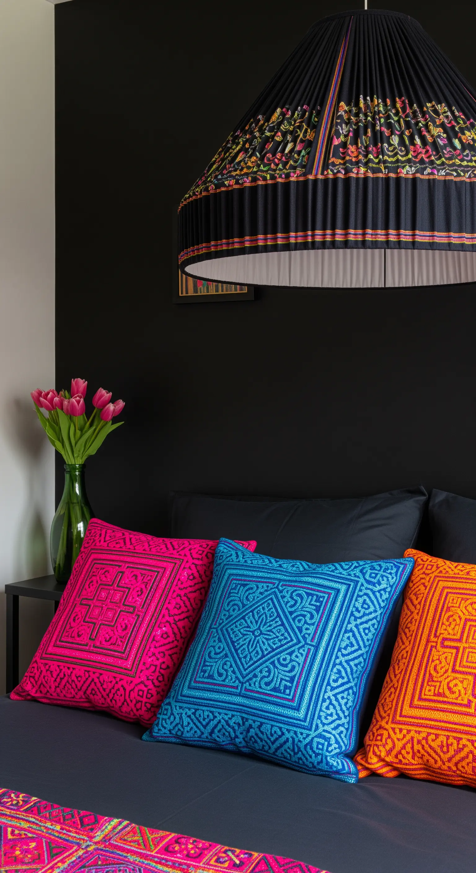Cuscini ricamati con colori neon (fucsia, ciano) su un letto con lenzuola nere e parete scura.