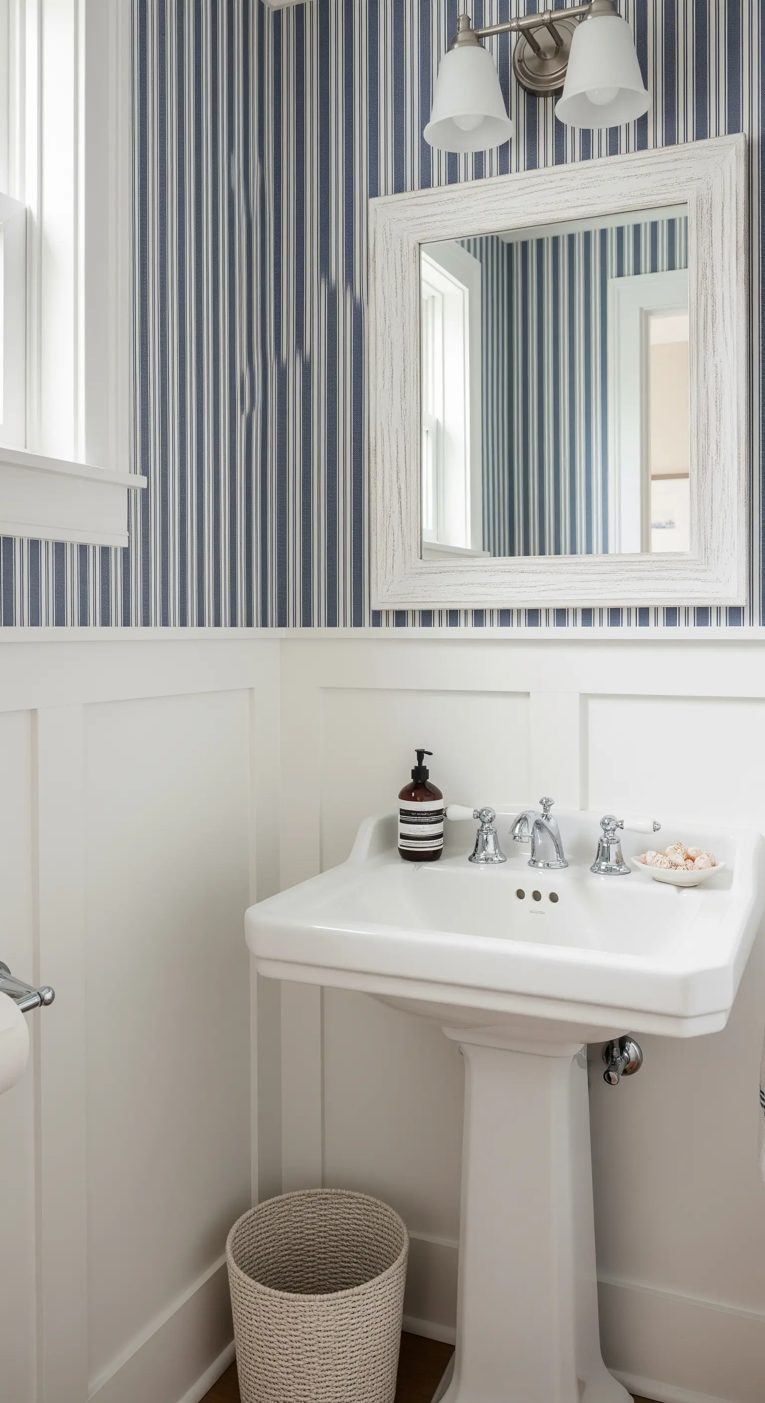 Lavabo a colonna con carta da parati a righe blu e bianche e specchio decapato.