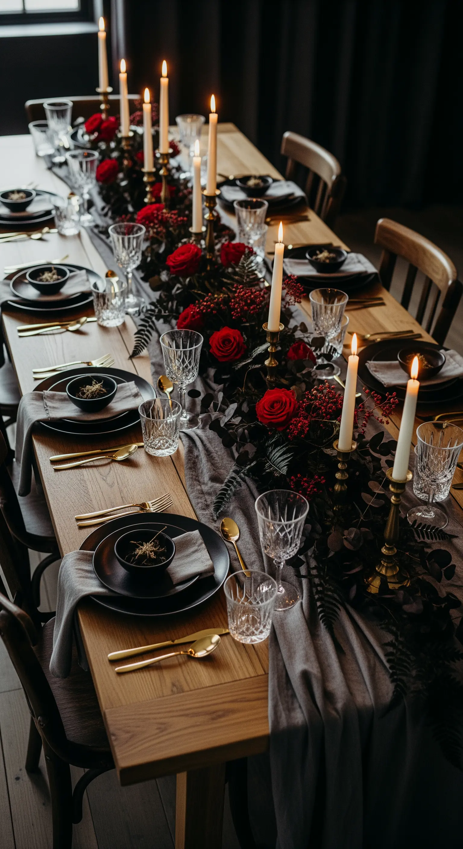 Tavola autunnale con runner grigio, rose rosse, piatti neri e posate dorate.