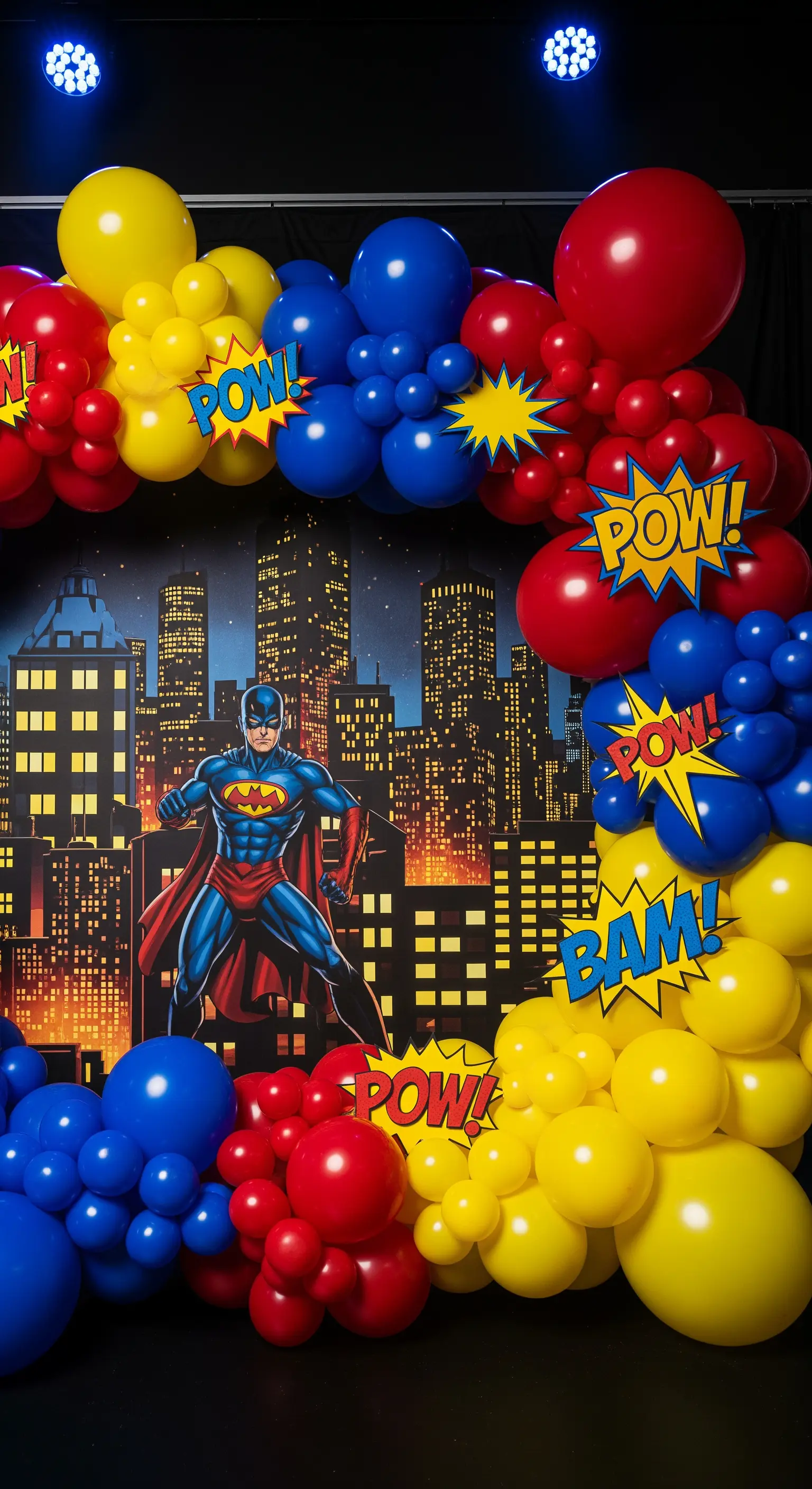 Decorazione a tema supereroi con palloncini colorati e backdrop di una città notturna.