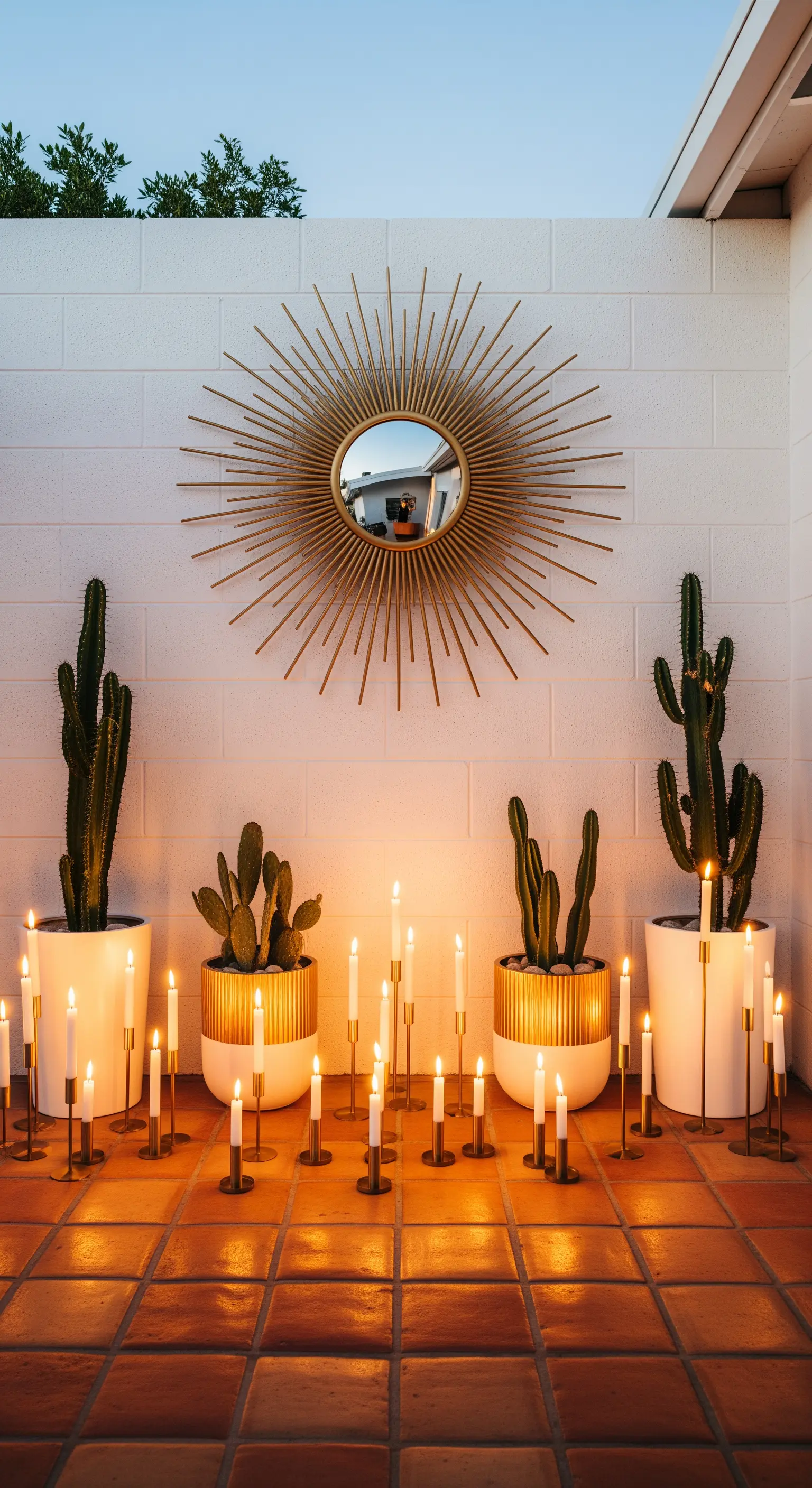 Patio con specchio a raggiera dorato, cactus in vaso e candele sottili su candelieri.