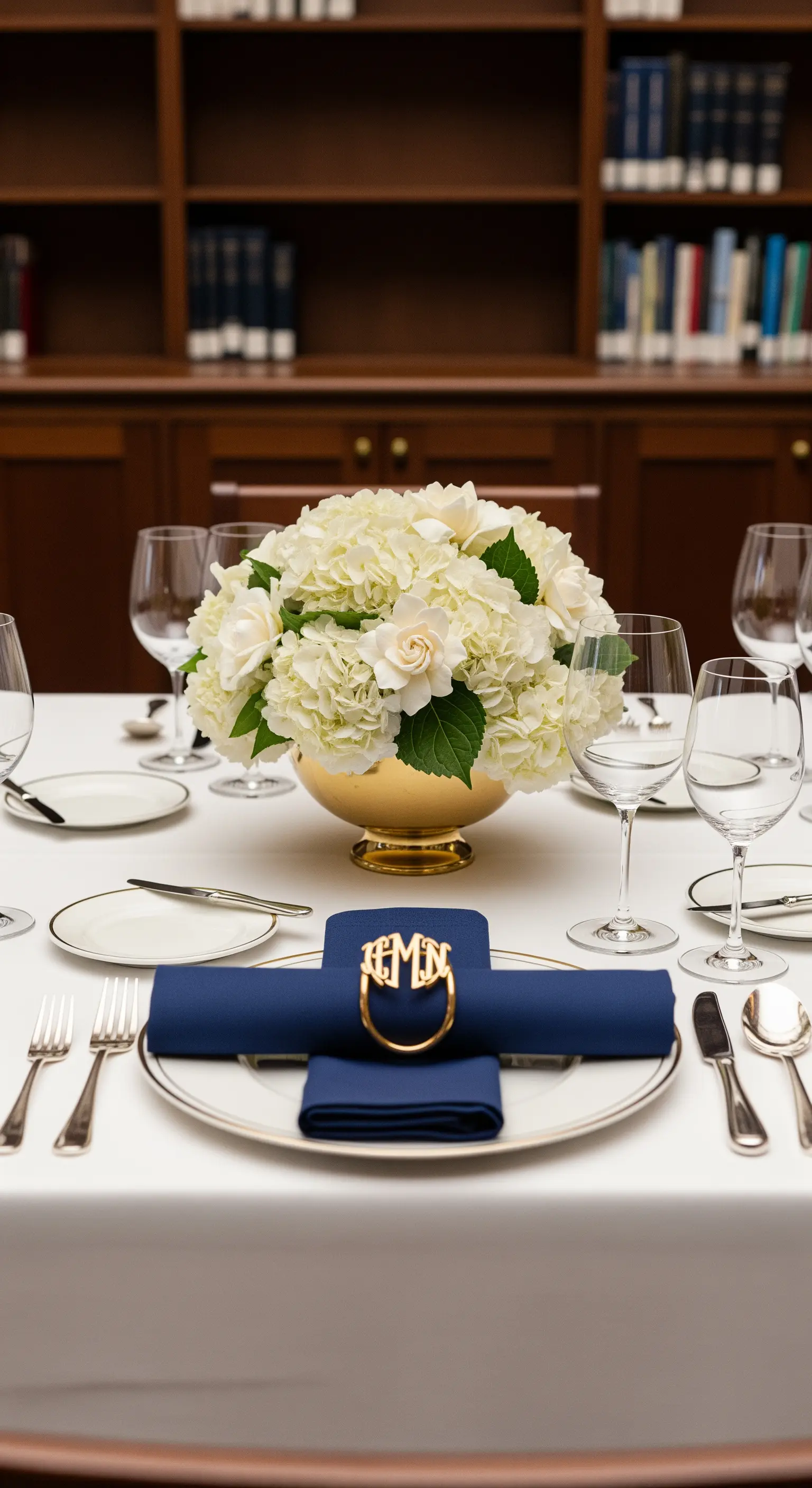 Tavola formale con tovaglioli blu navy e anello dorato con monogramma, fiori bianchi.