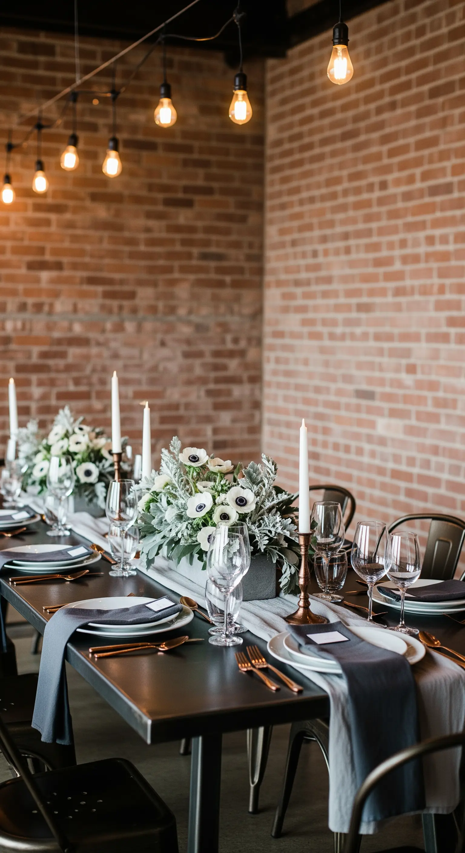 Tavola in stile industriale con mattoni a vista, posate in rame e anemoni bianchi.