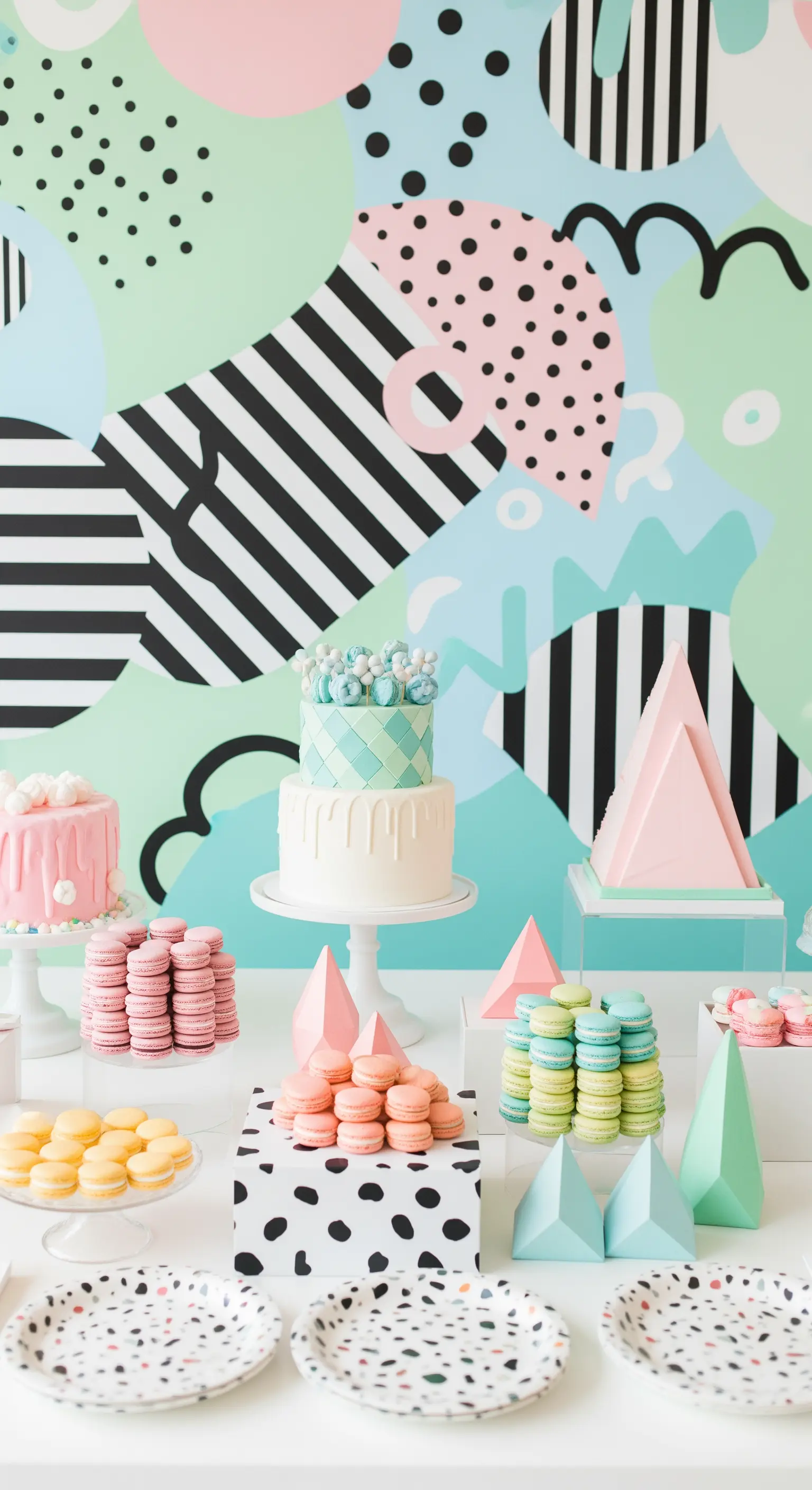 Tavolo da buffet in stile Memphis con torte e macarons su sfondo geometrico e colorato.