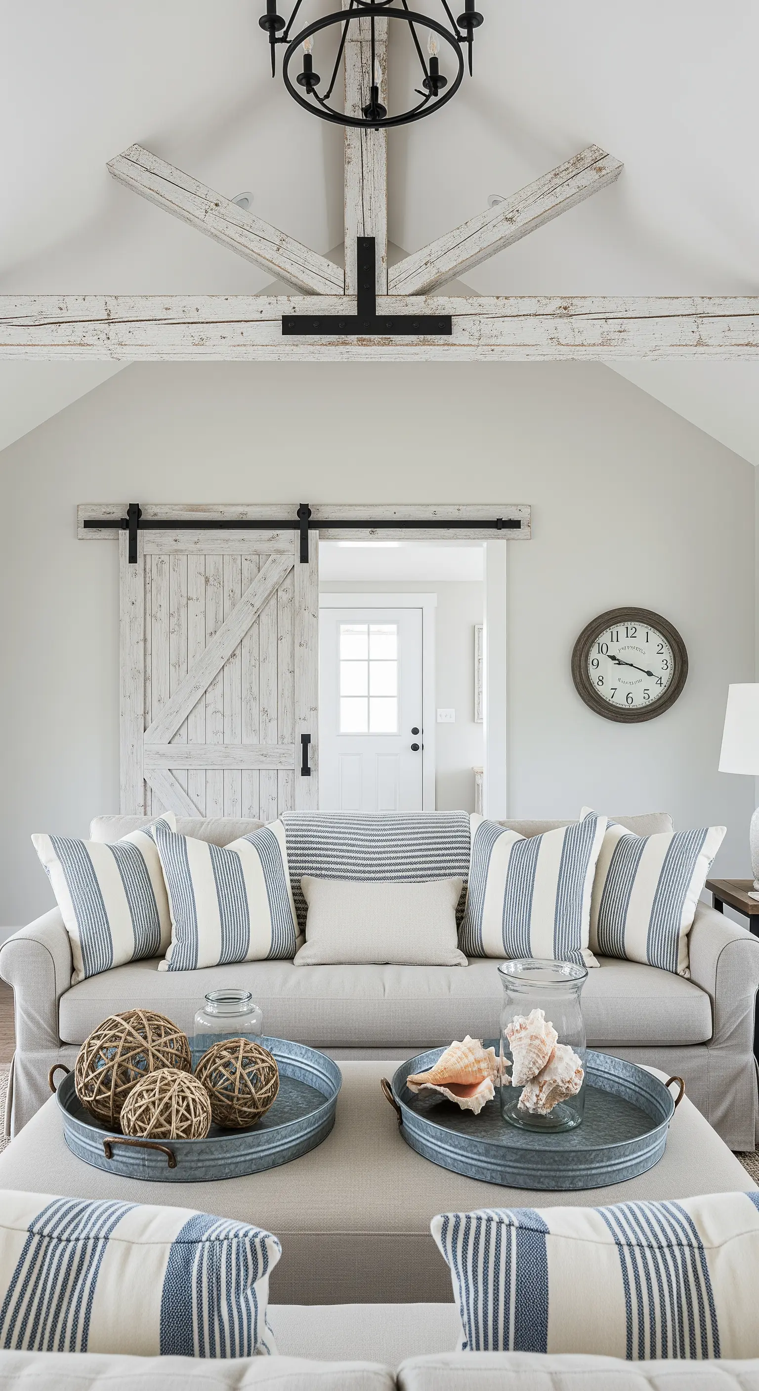 Divano neutro con cuscini a righe e porta da fienile in legno sbiancato.