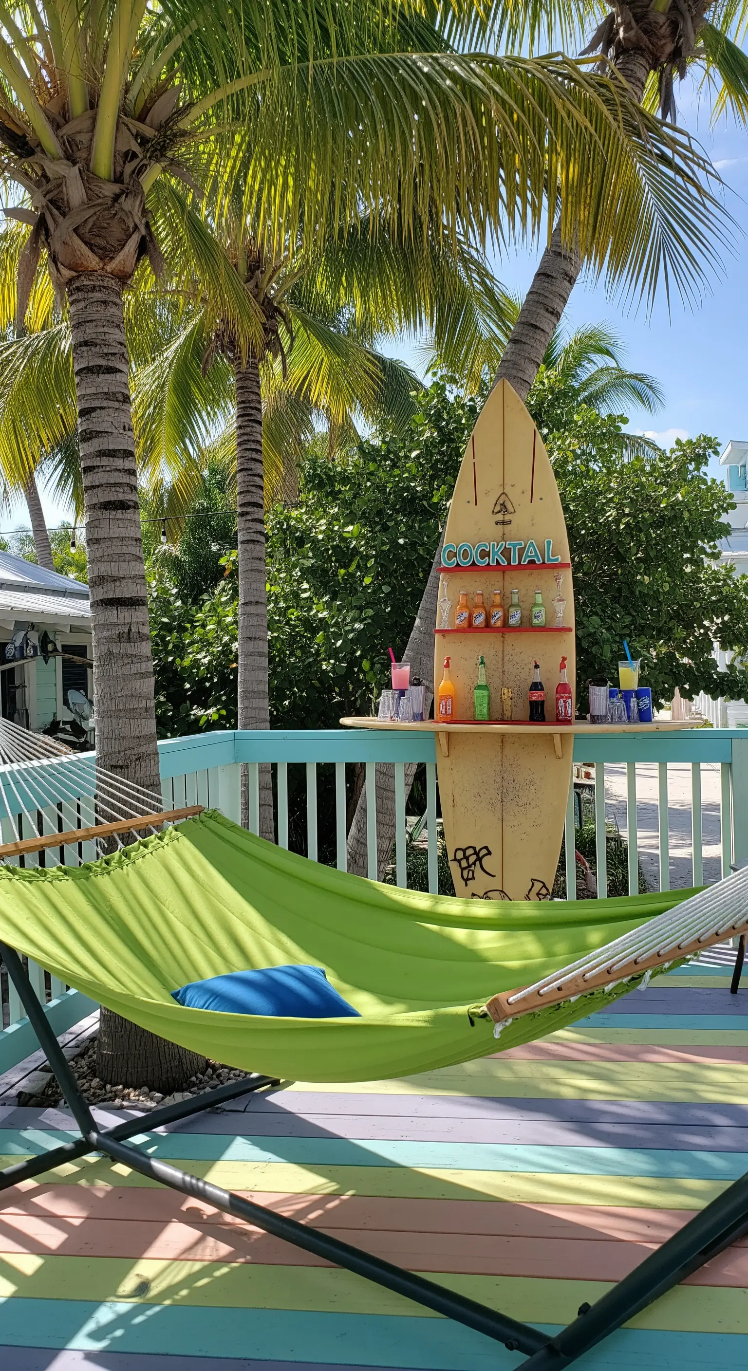 Portico a tema surf con bar ricavato da una tavola, amaca verde e pavimento a righe colorate