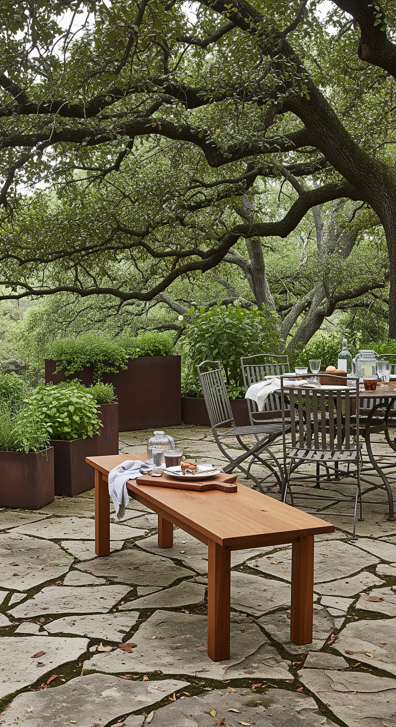 Panca in teak e tavolo da pranzo in metallo, circondati da fioriere in acciaio Corten.