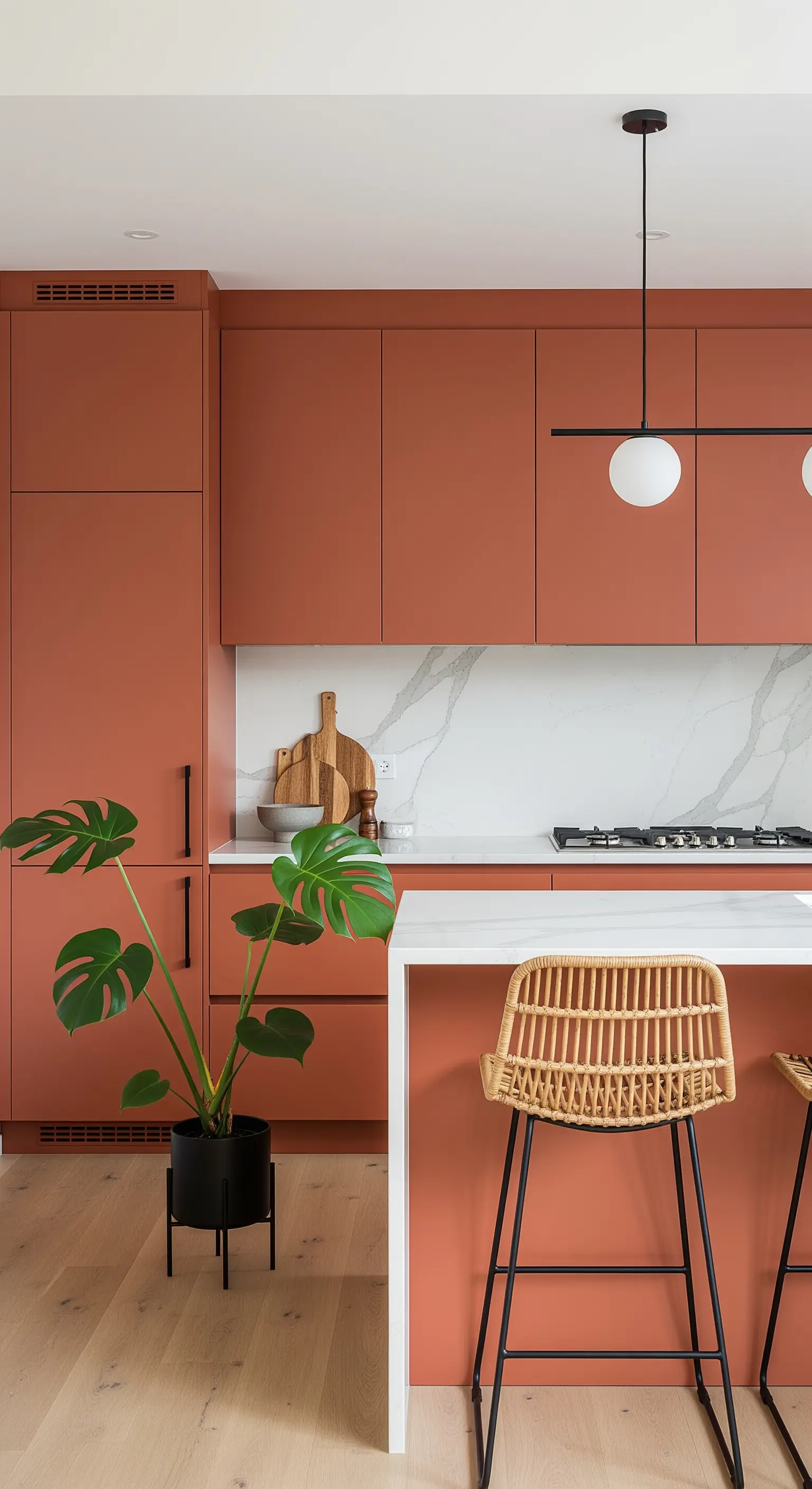 Cucina moderna con mobili color terracotta, paraschizzi in marmo e pianta di monstera.