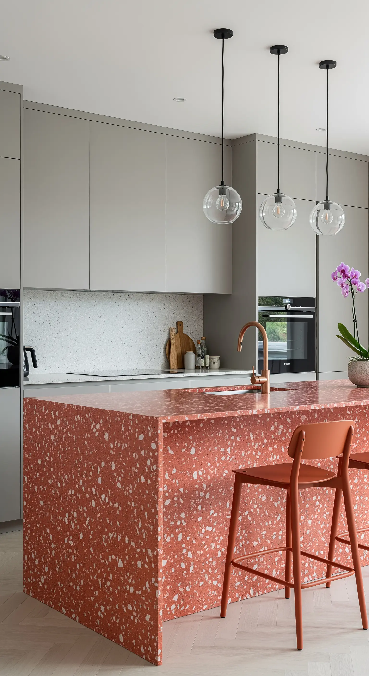Cucina moderna con isola e sgabelli in terrazzo color terracotta e mobili grigi.