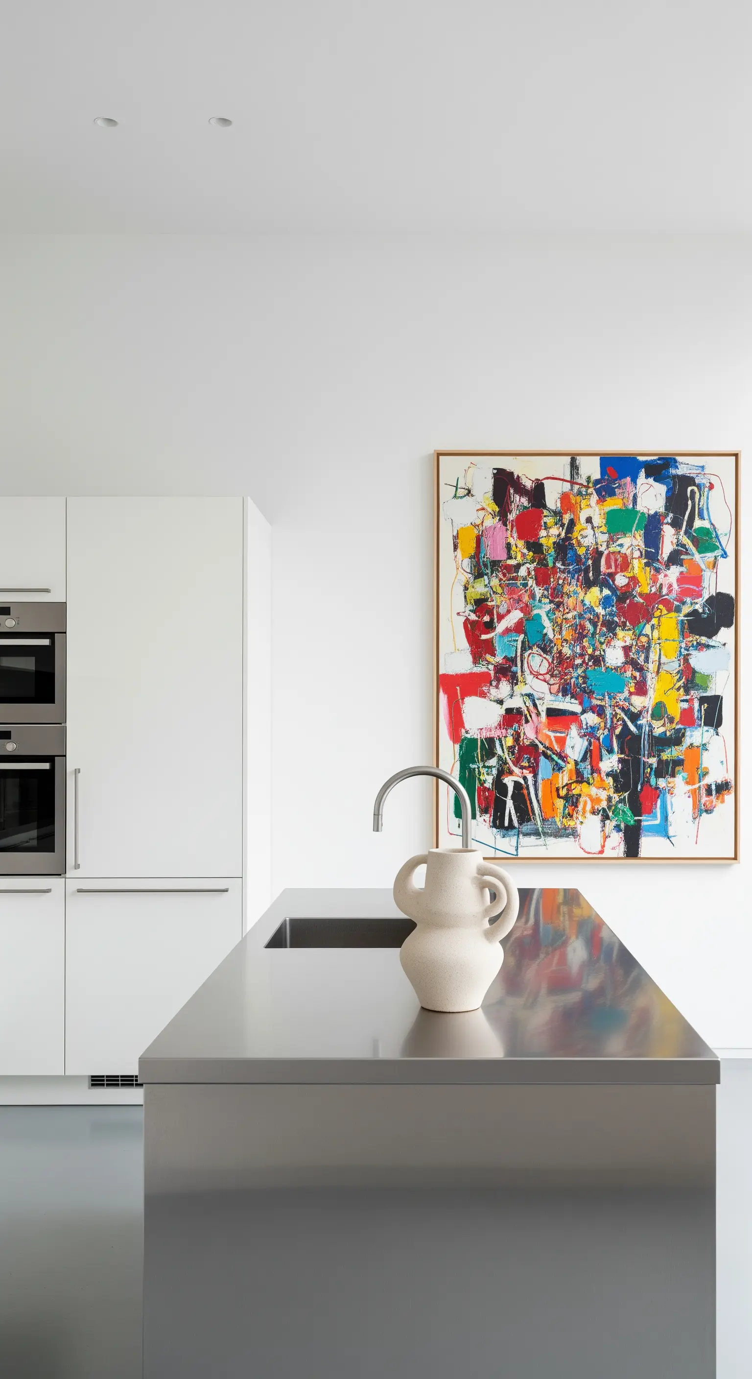 Isola cucina in acciaio inox con un grande quadro astratto e colorato appeso alla parete.
