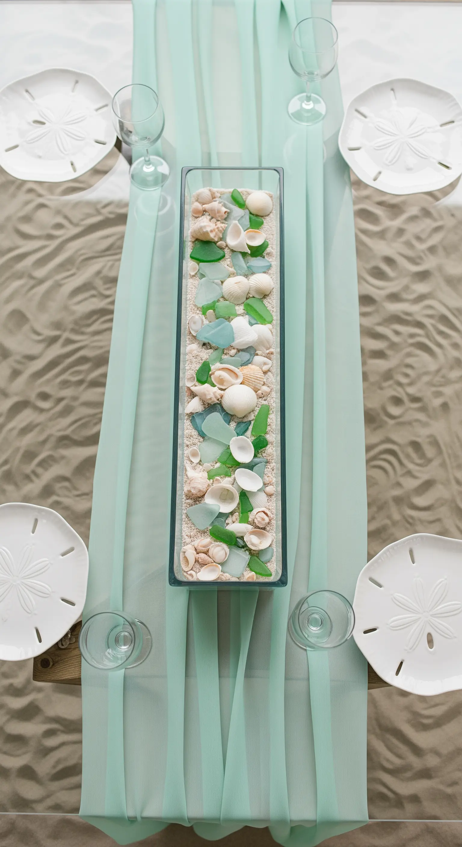 Runner in chiffon verde acqua con centrotavola in vetro riempito di sabbia e conchiglie.
