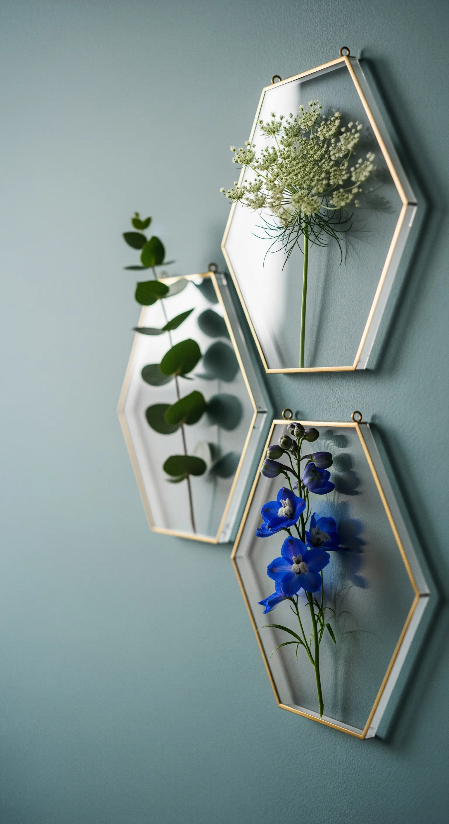 Tre cornici esagonali dorate con eucalipto, fiordaliso e fiori bianchi.
