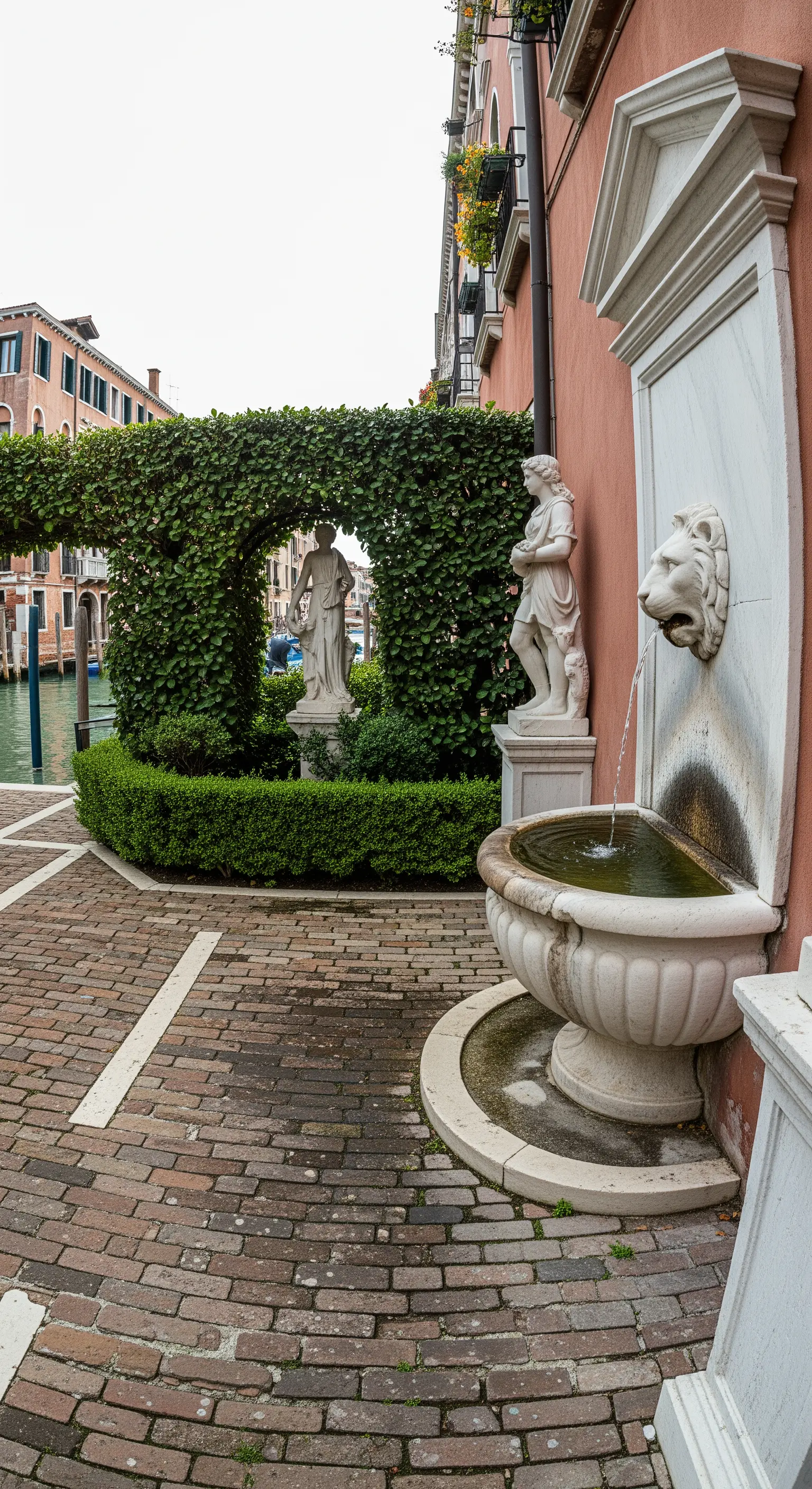 Angolo di un cortile a Venezia con fontana a mascherone, statue e un arco di edera.
