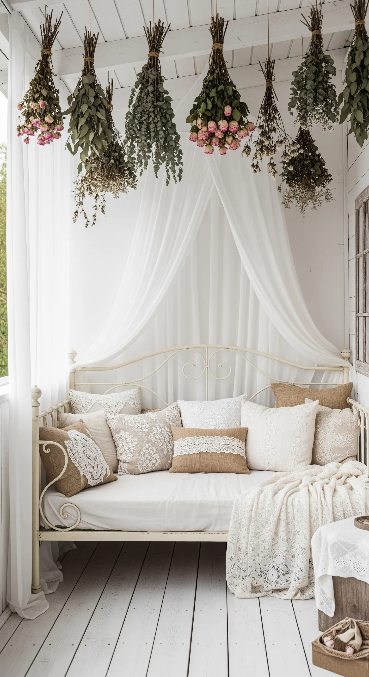 Lettino bianco da esterno con cuscini e una tenda a baldacchino sotto mazzi di fiori secchi appesi.