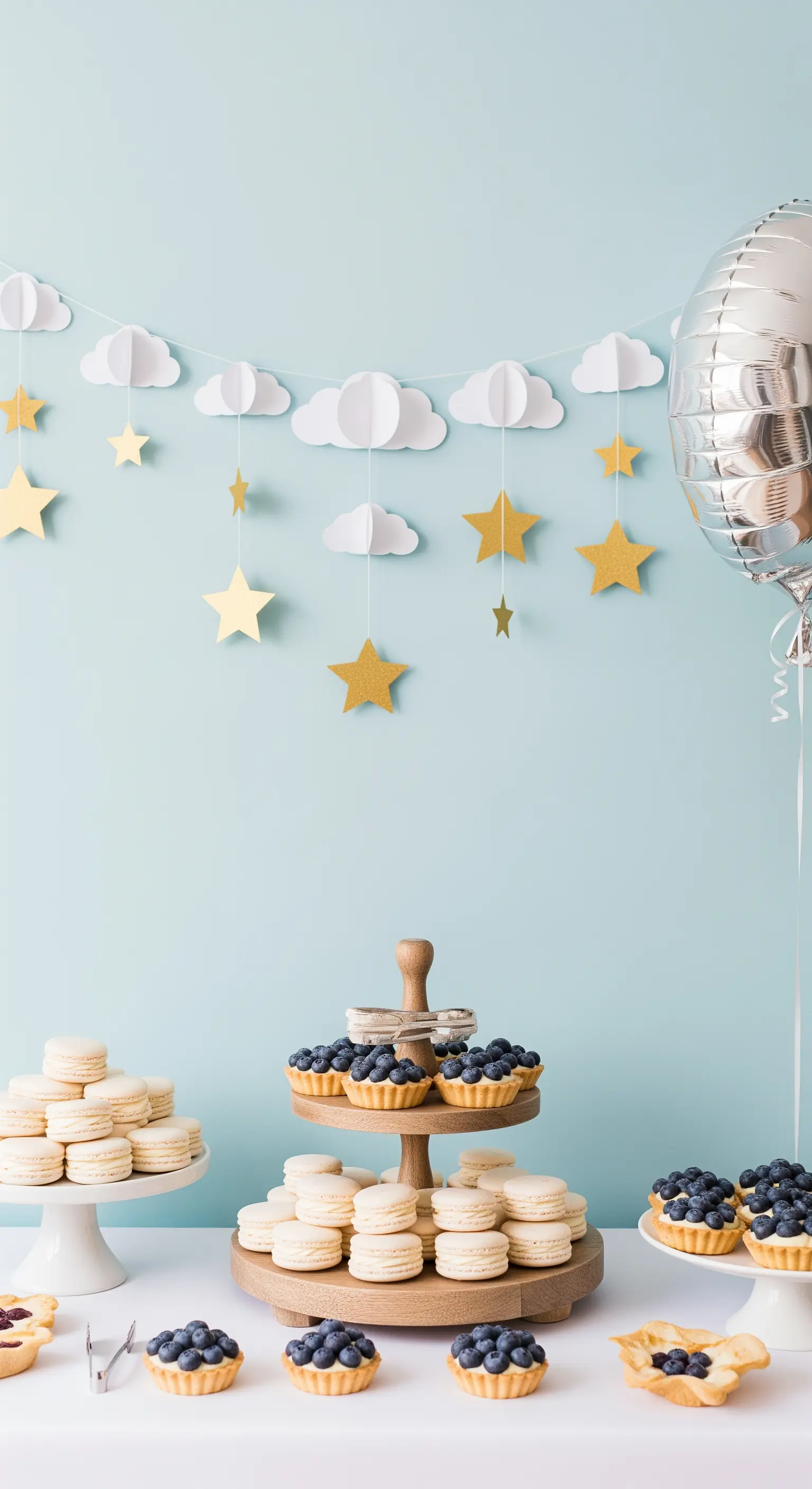 Tavolo da buffet con dolci bianchi sotto una ghirlanda di carta con nuvole e stelle dorate.