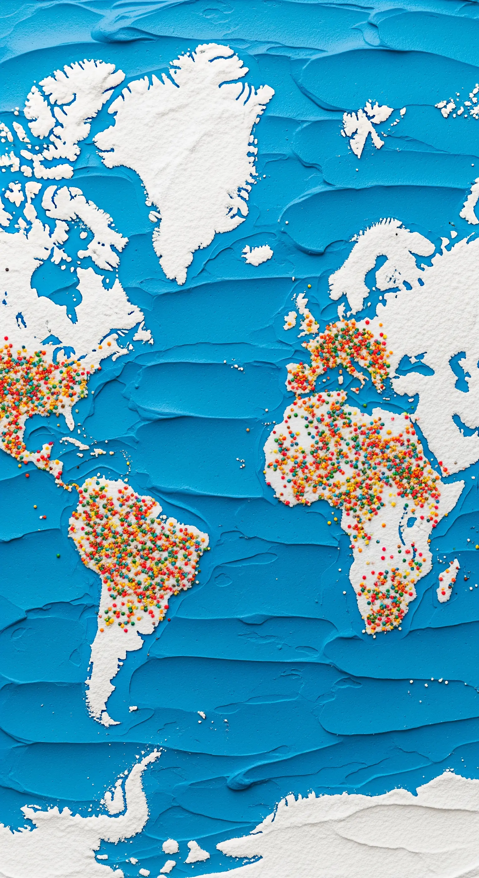 Mappa del mondo creata su una torta con glassa blu, zucchero a velo e zuccherini colorati.