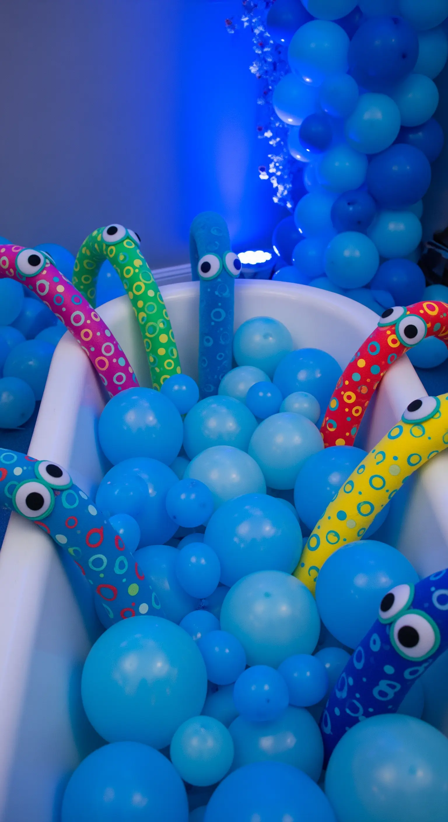 Vasca da bagno piena di palloncini blu da cui emergono tentacoli di mostri colorati.