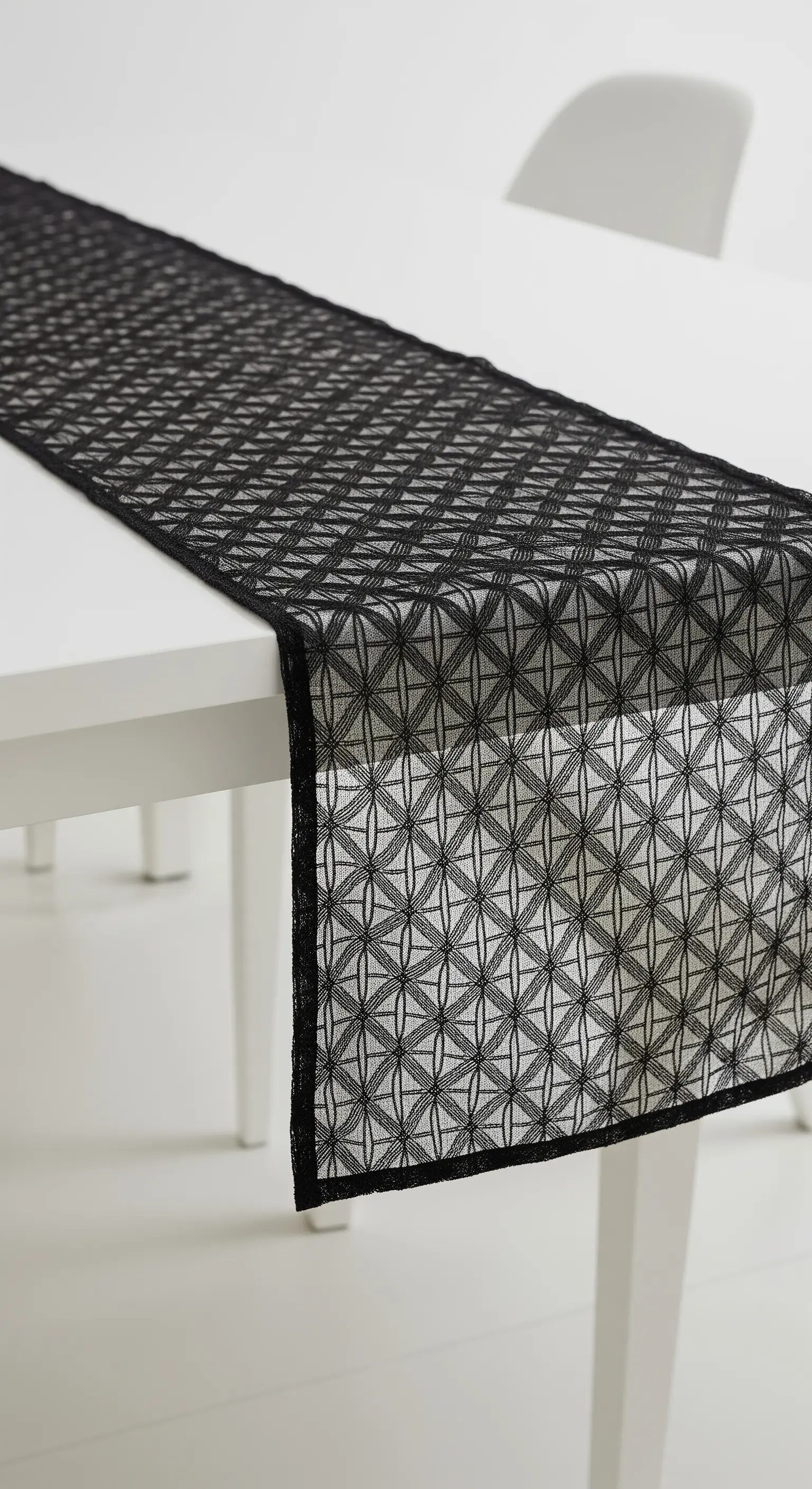 Runner nero in pizzo con motivo geometrico su un tavolo da pranzo bianco.