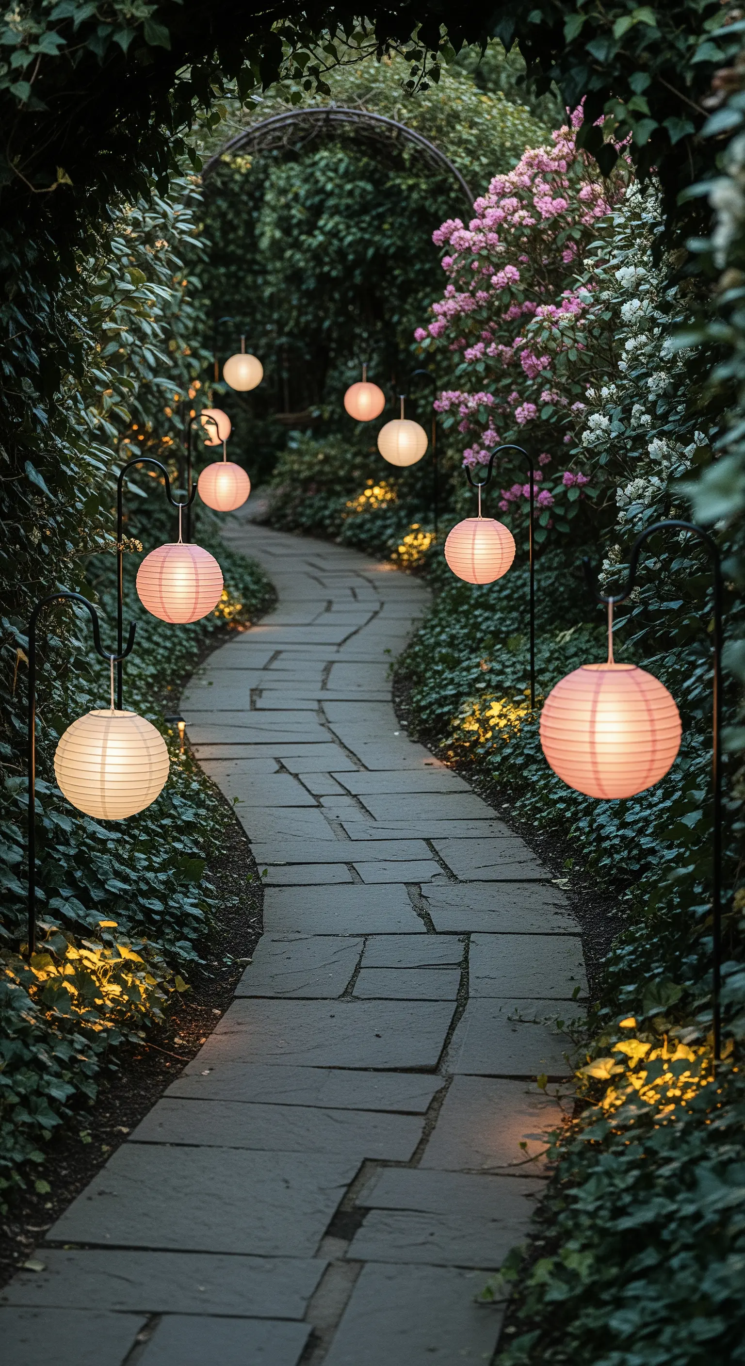 Sentiero in pietra in un giardino rigoglioso, illuminato da lanterne di carta rosa.