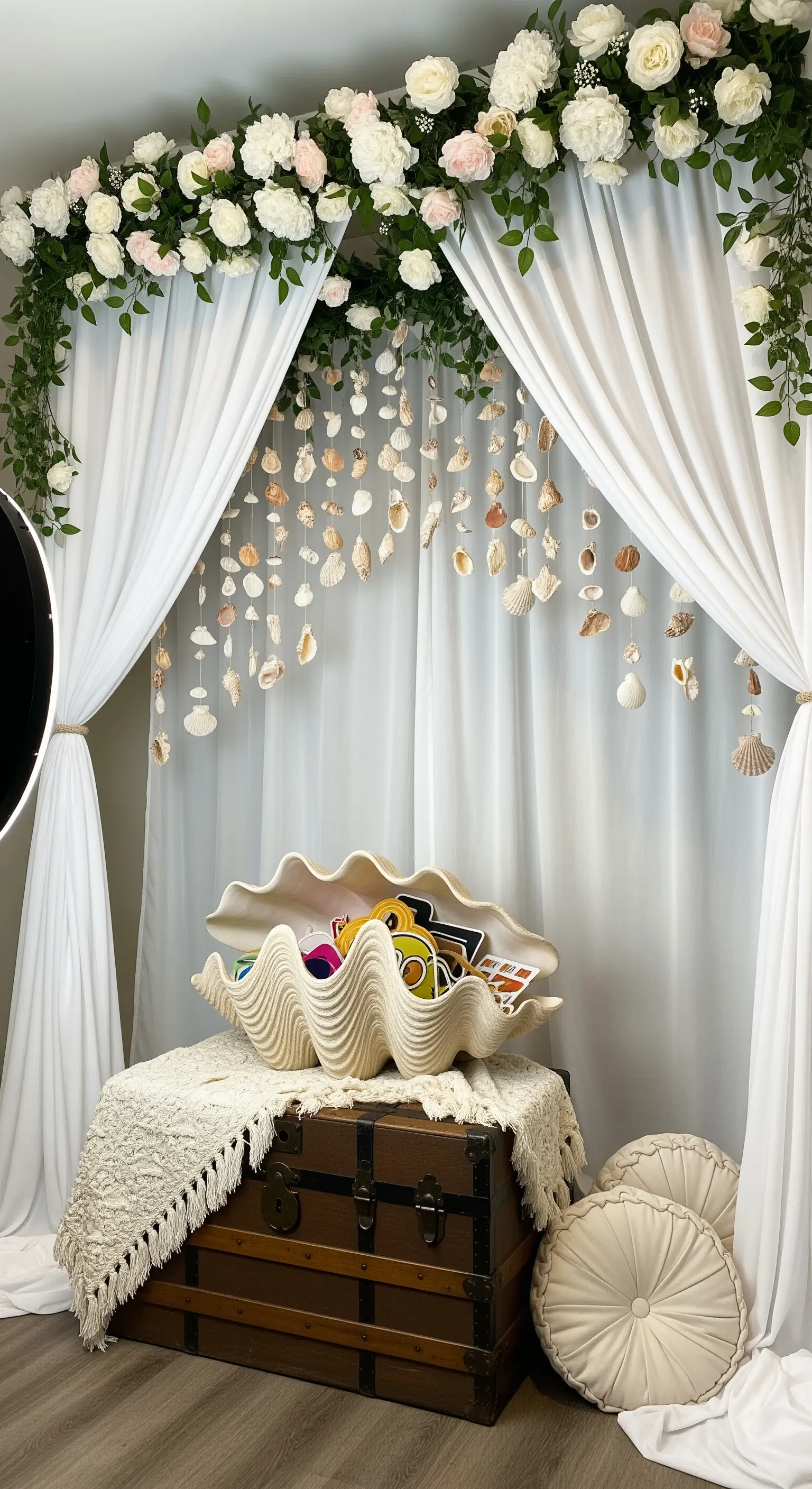 Photo booth con tende bianche, ghirlande di conchiglie pendenti e una grande conchiglia decorativa.