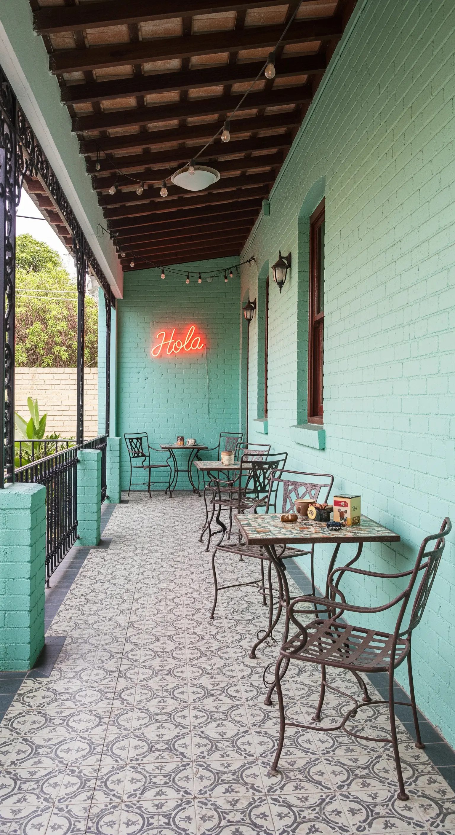 Veranda con parete verde menta, pavimento a piastrelle decorate e tavolini in ferro battuto.