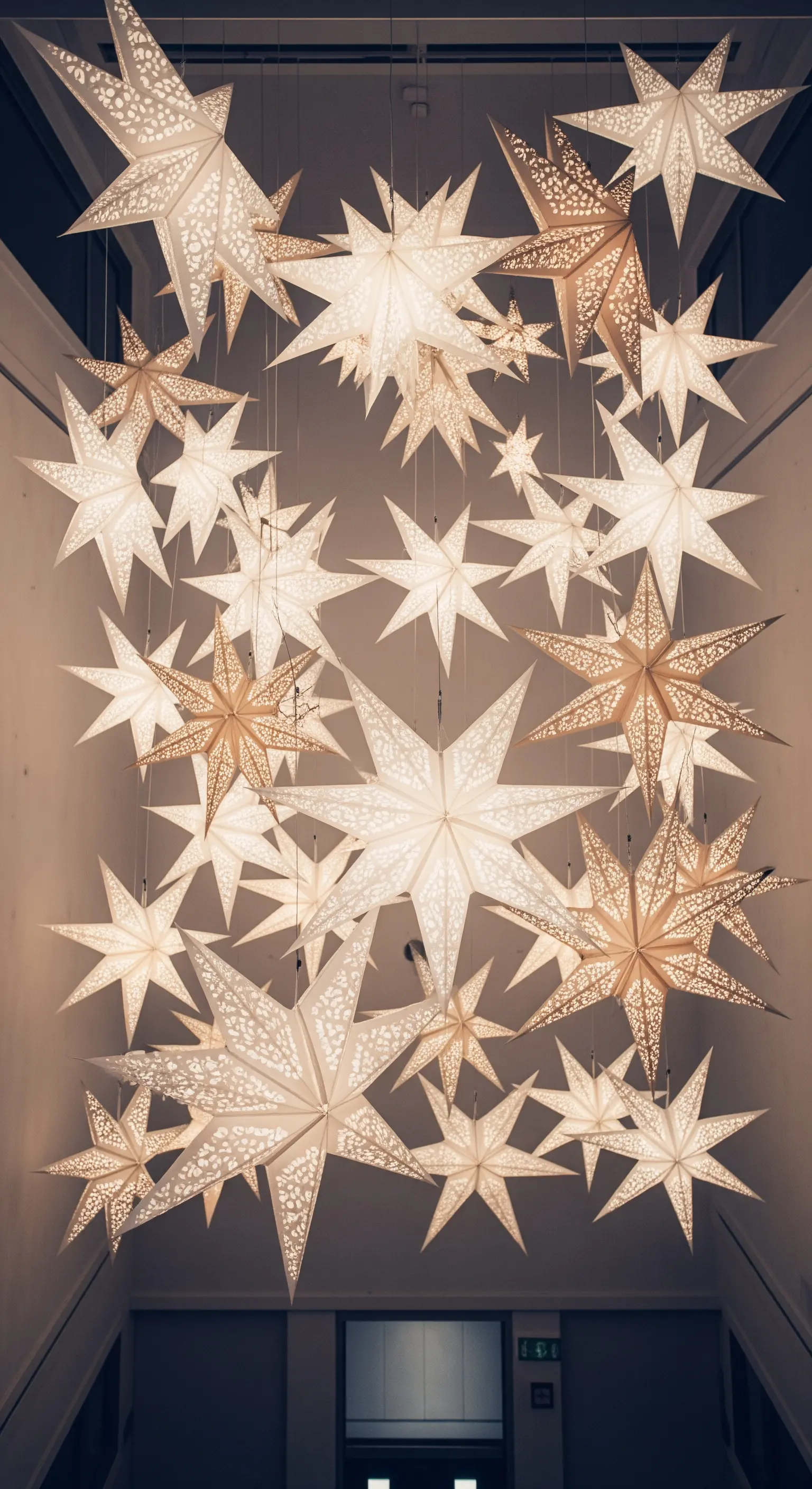 Installazione a soffitto con decine di stelle di carta luminose di varie dimensioni.