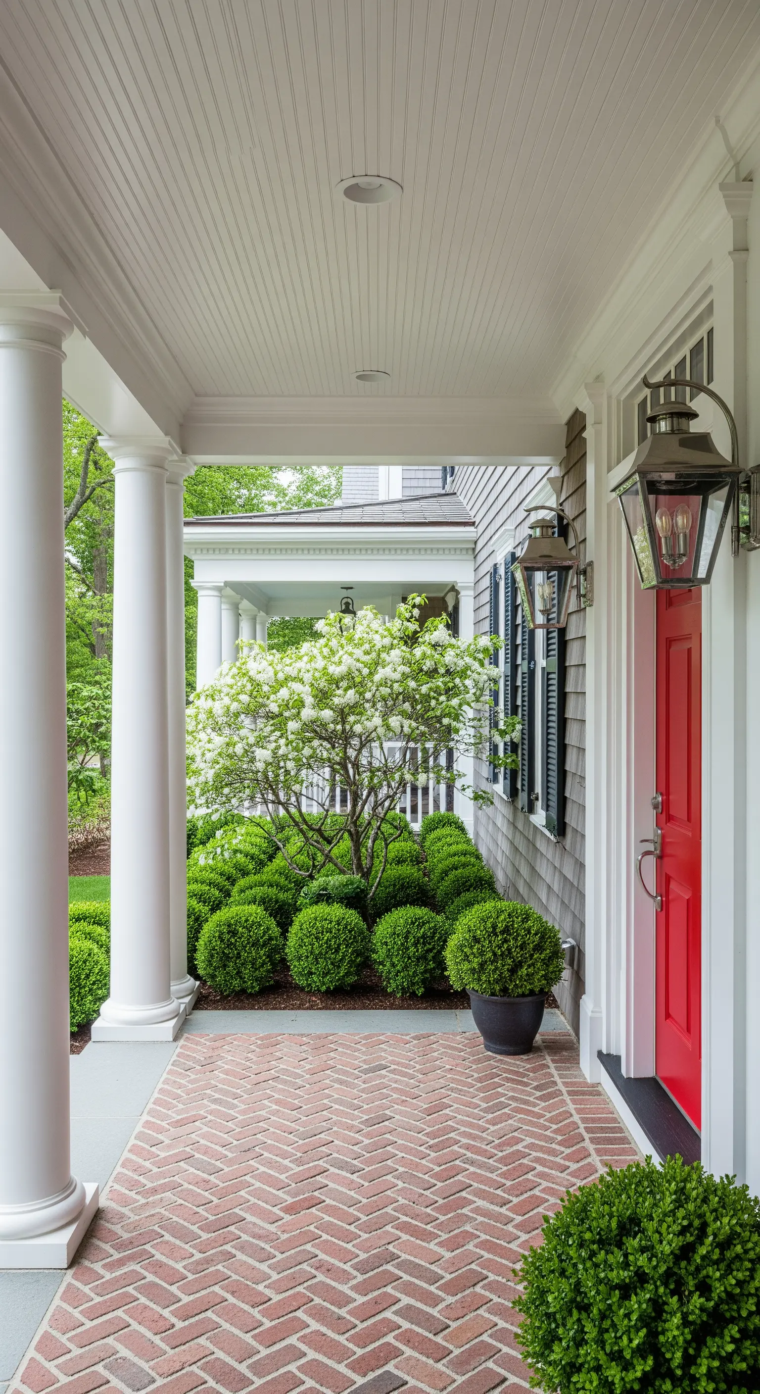 Portico con colonne bianche, pavimento in mattoni a spina di pesce e una vivace porta rossa.
