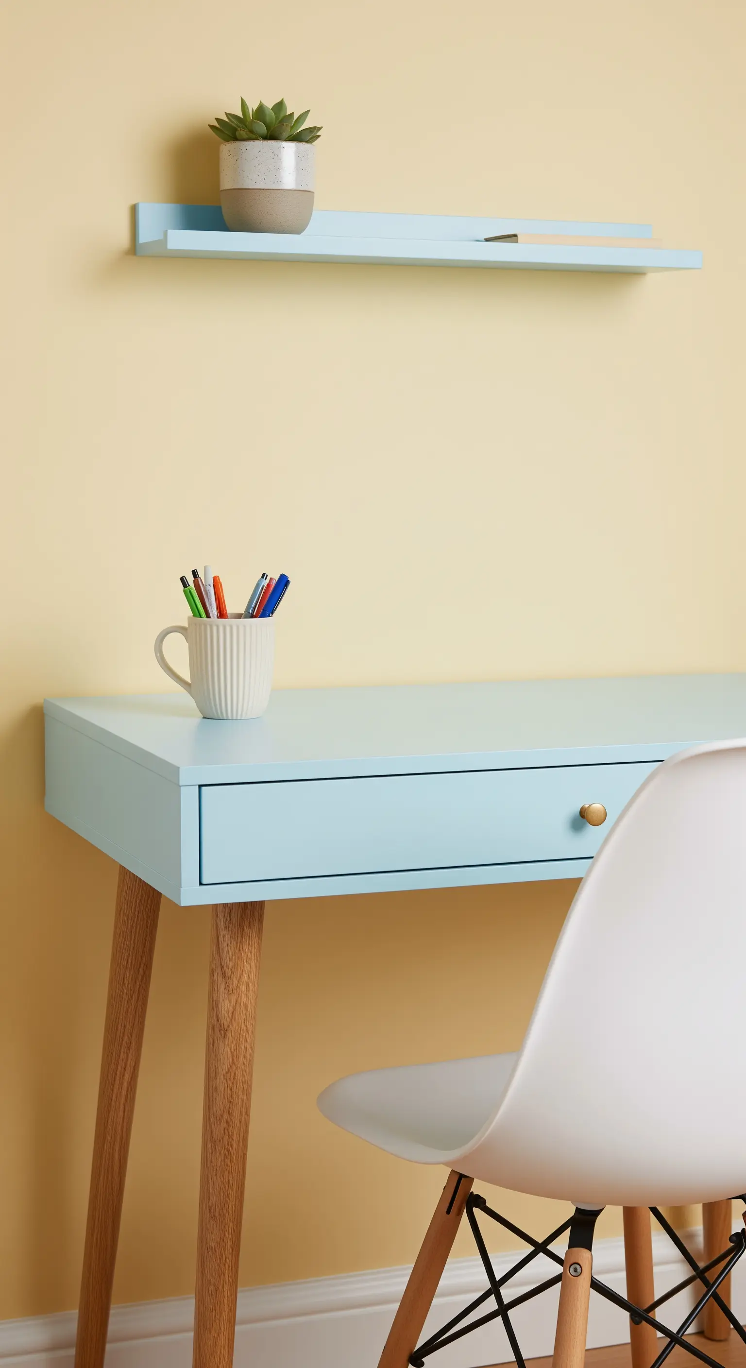 Scrivania azzurro pastello con gambe in legno chiaro contro una parete giallo burro.