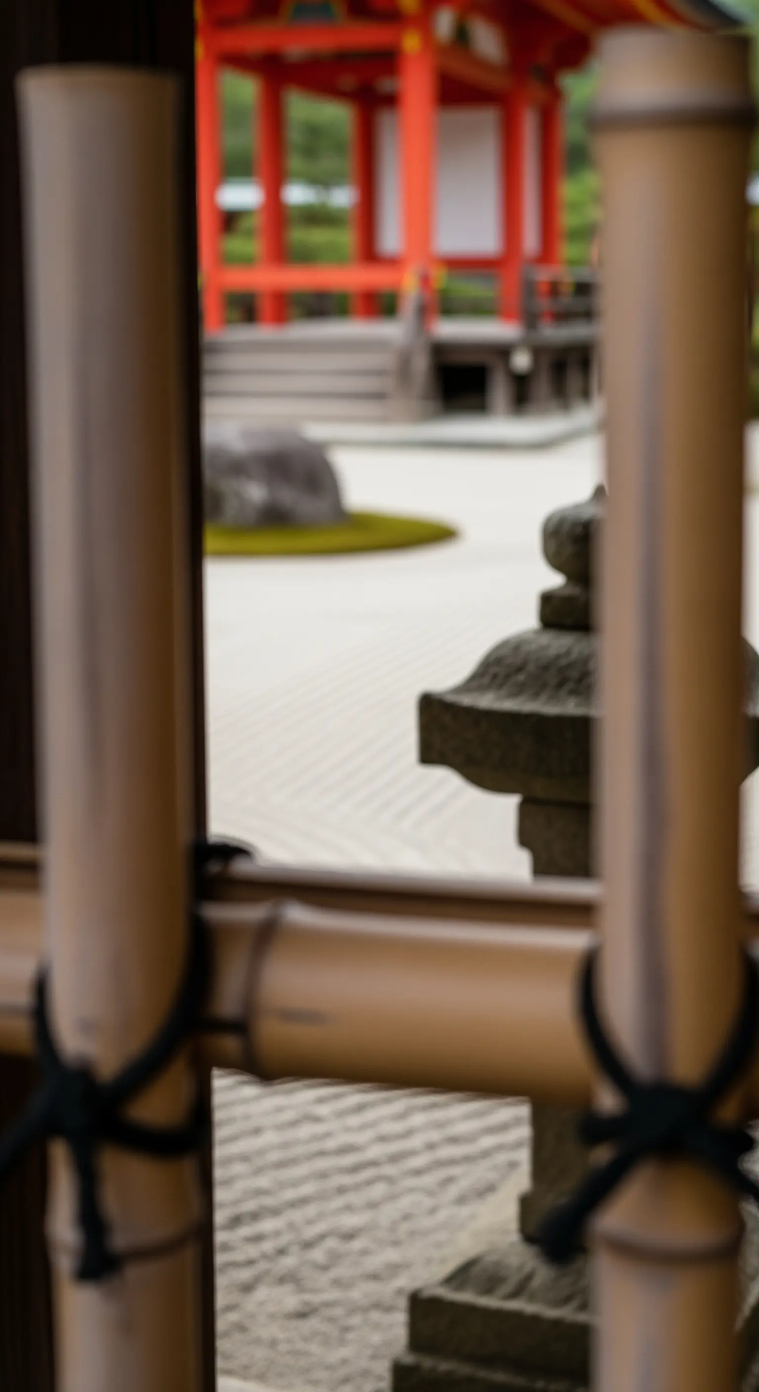 Vista sfocata di un giardino zen attraverso una staccionata di bambù in primo piano.