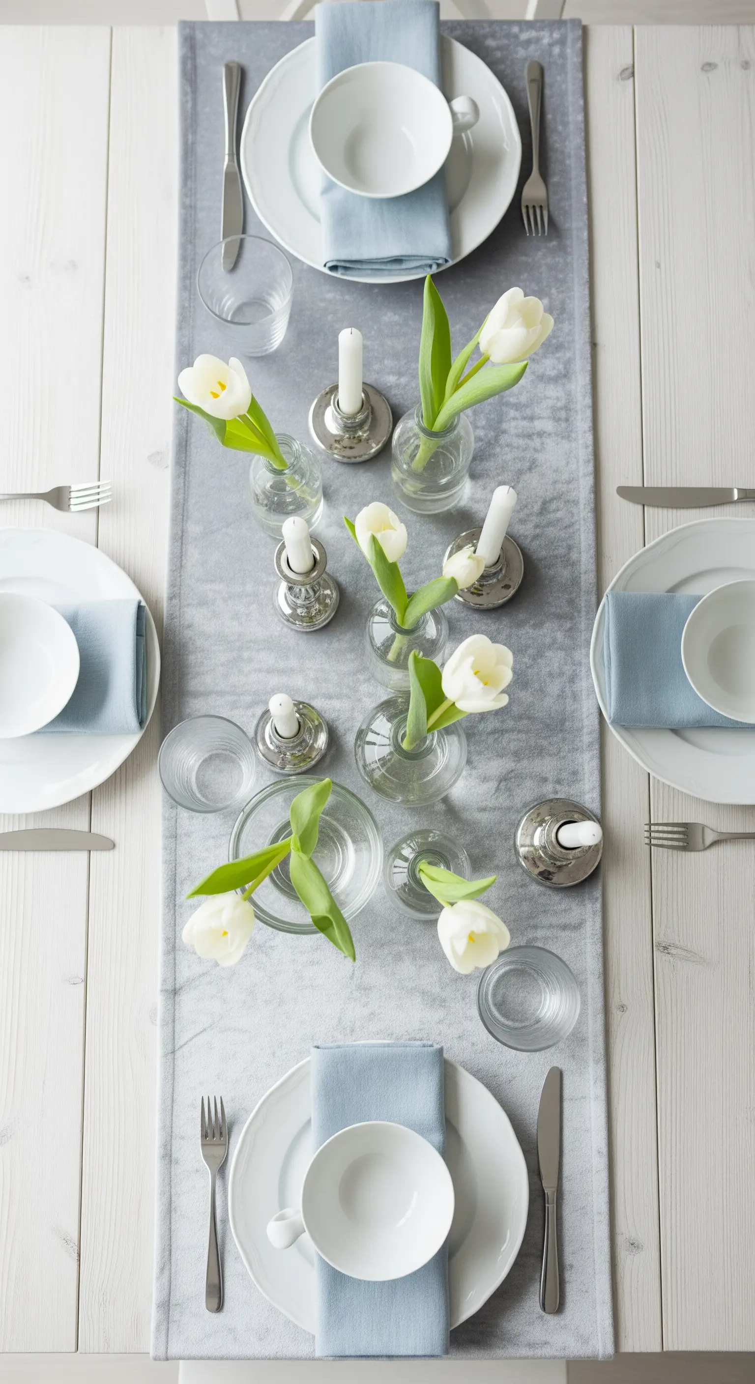 Tavola minimalista con runner in velluto grigio, tulipani bianchi e portacandele argento.