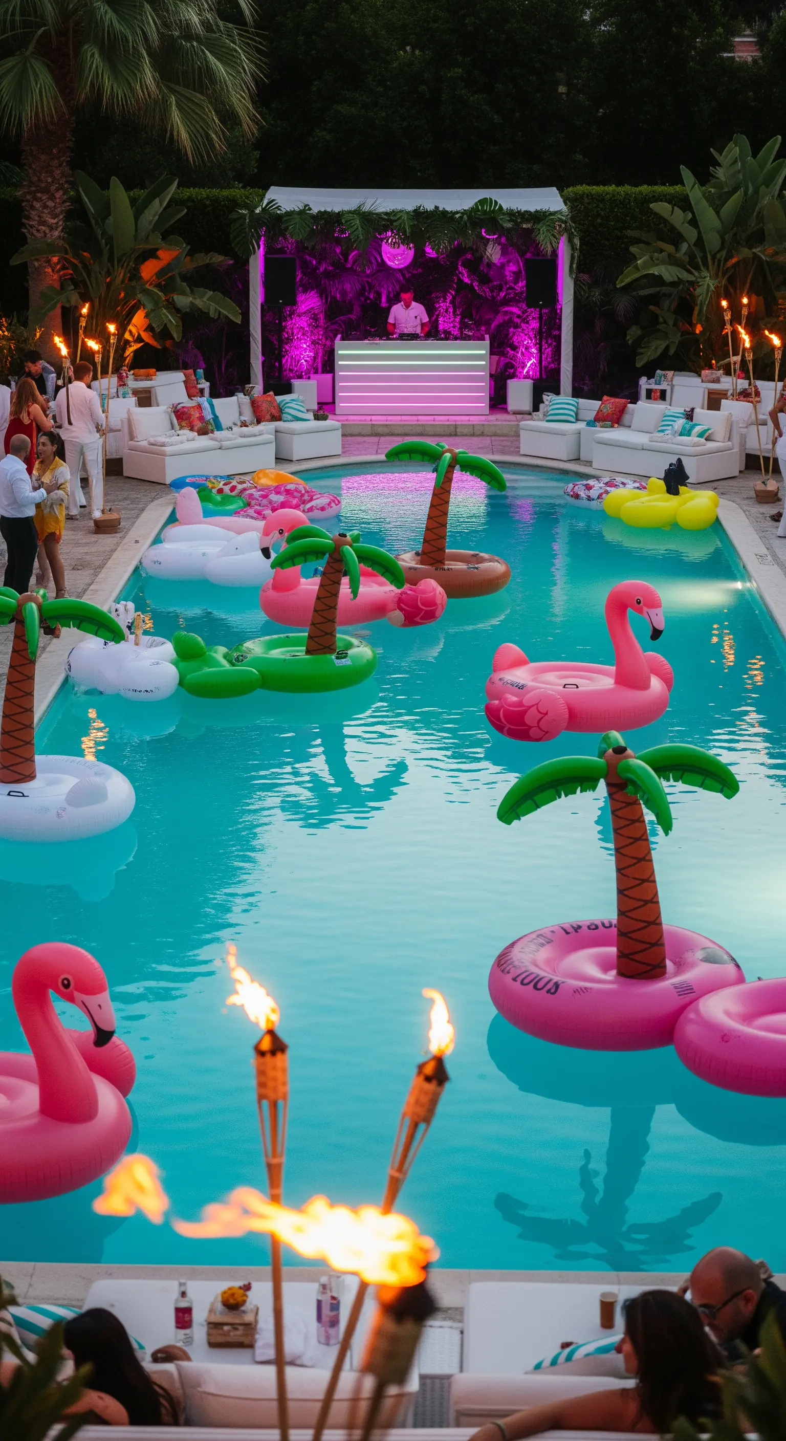 Pool party notturna con DJ set, luci fucsia, gonfiabili a forma di fenicottero e torce accese.