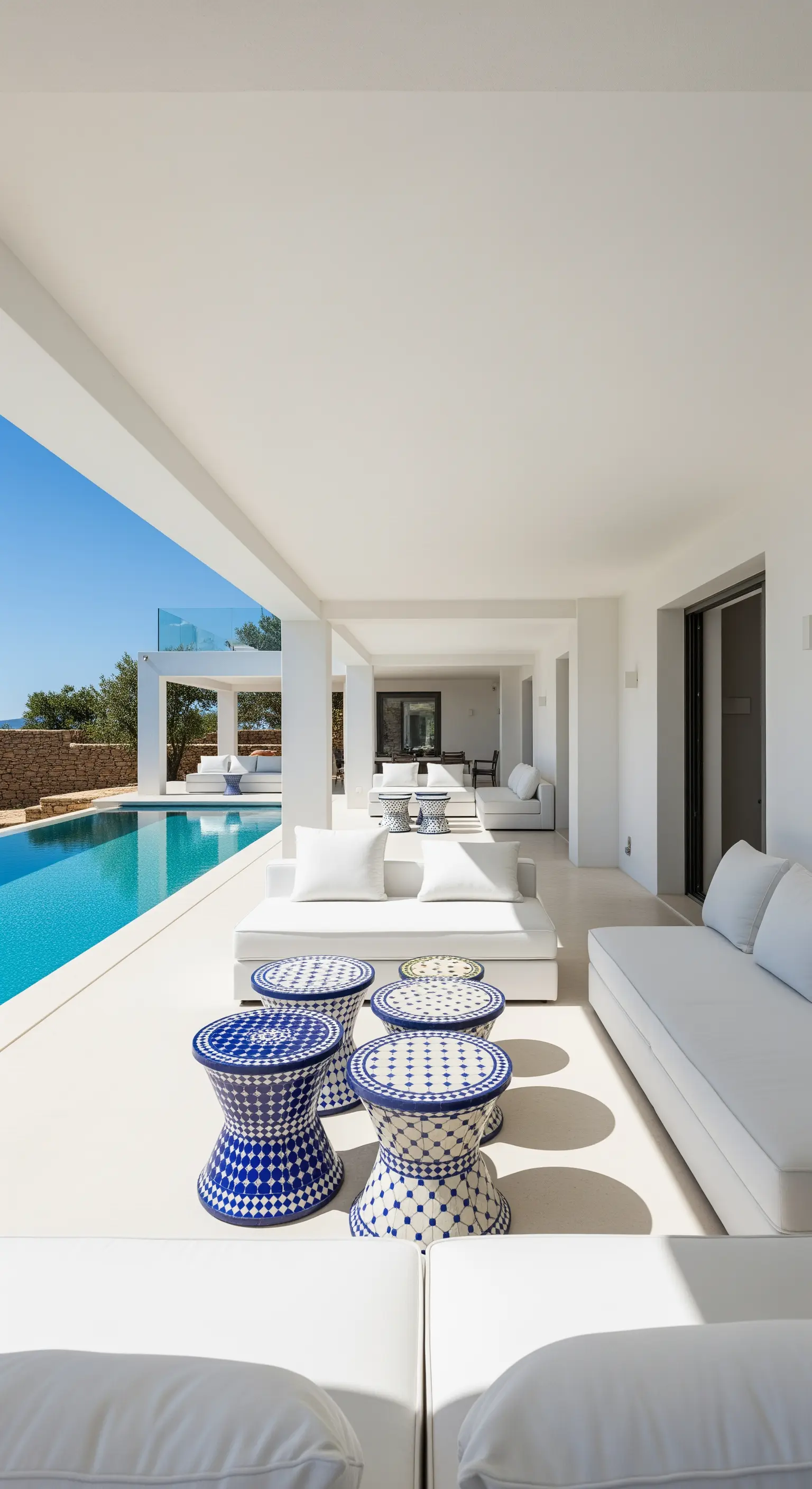 Bordo piscina moderno con divani bianchi e sgabelli a mosaico blu e bianchi.