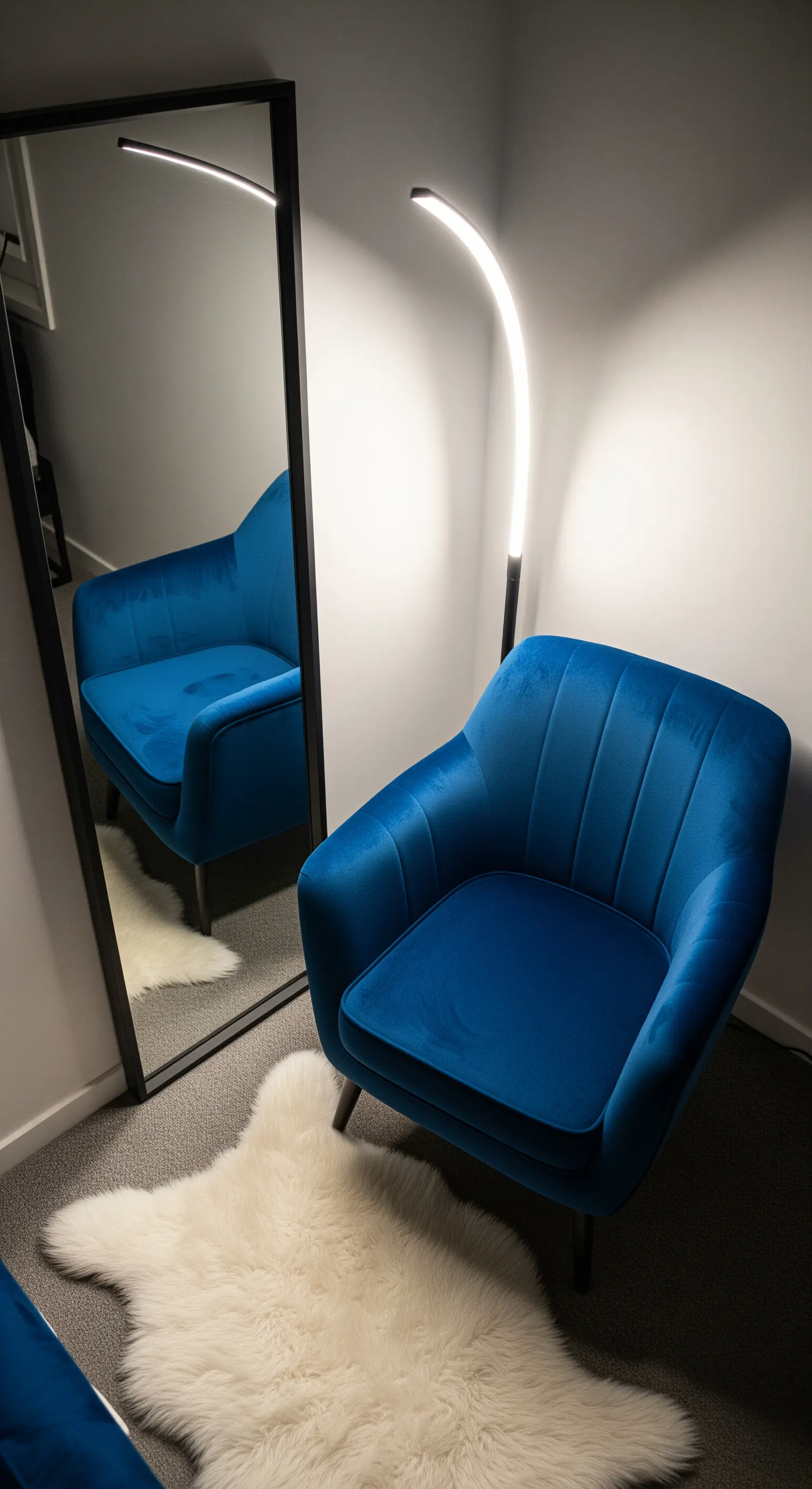 Poltrona in velluto blu accanto a uno specchio a figura intera, con lampada da terra a LED.