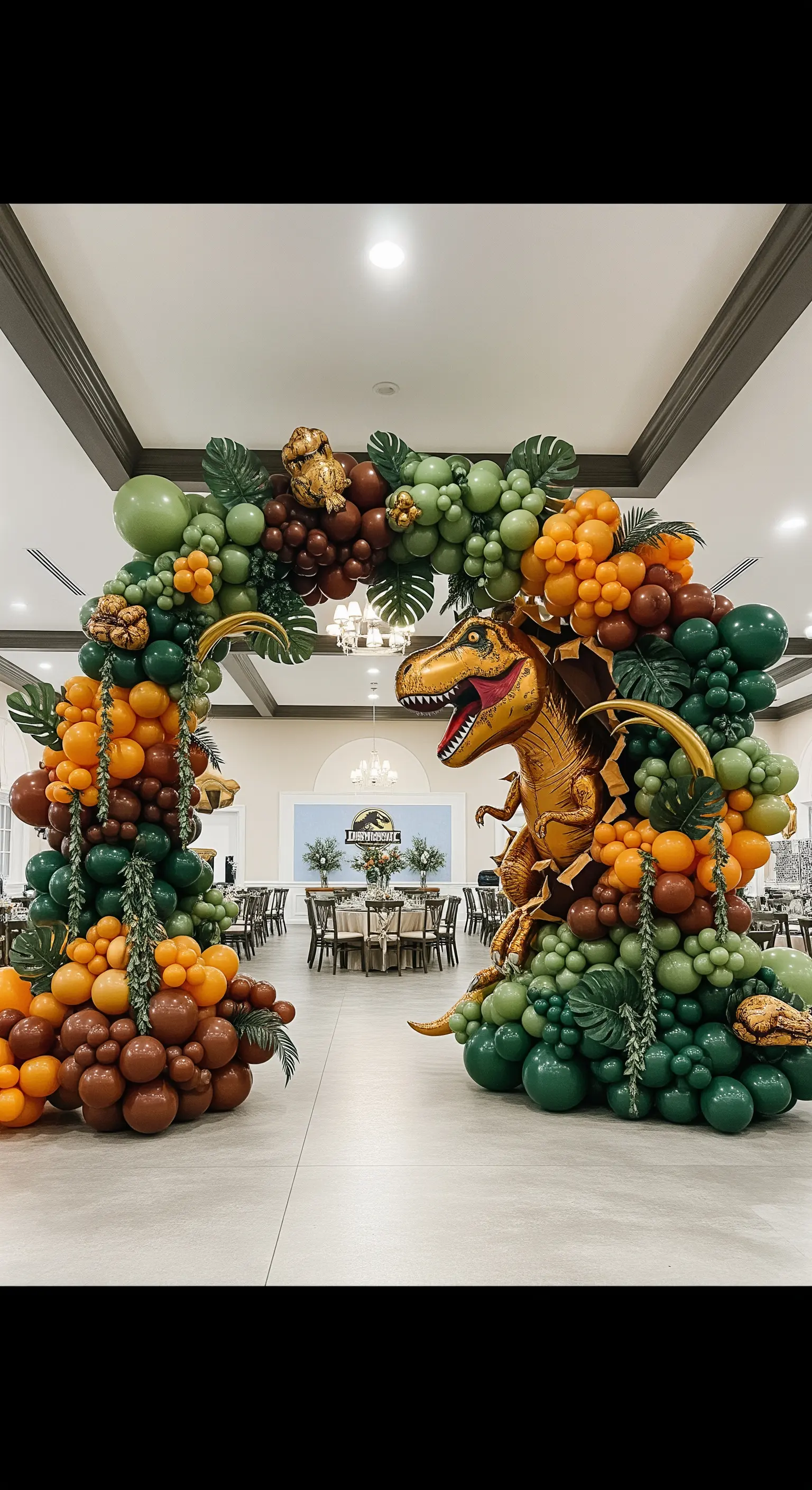 Grande arco di palloncini nei toni della terra con foglie tropicali e un T-Rex.