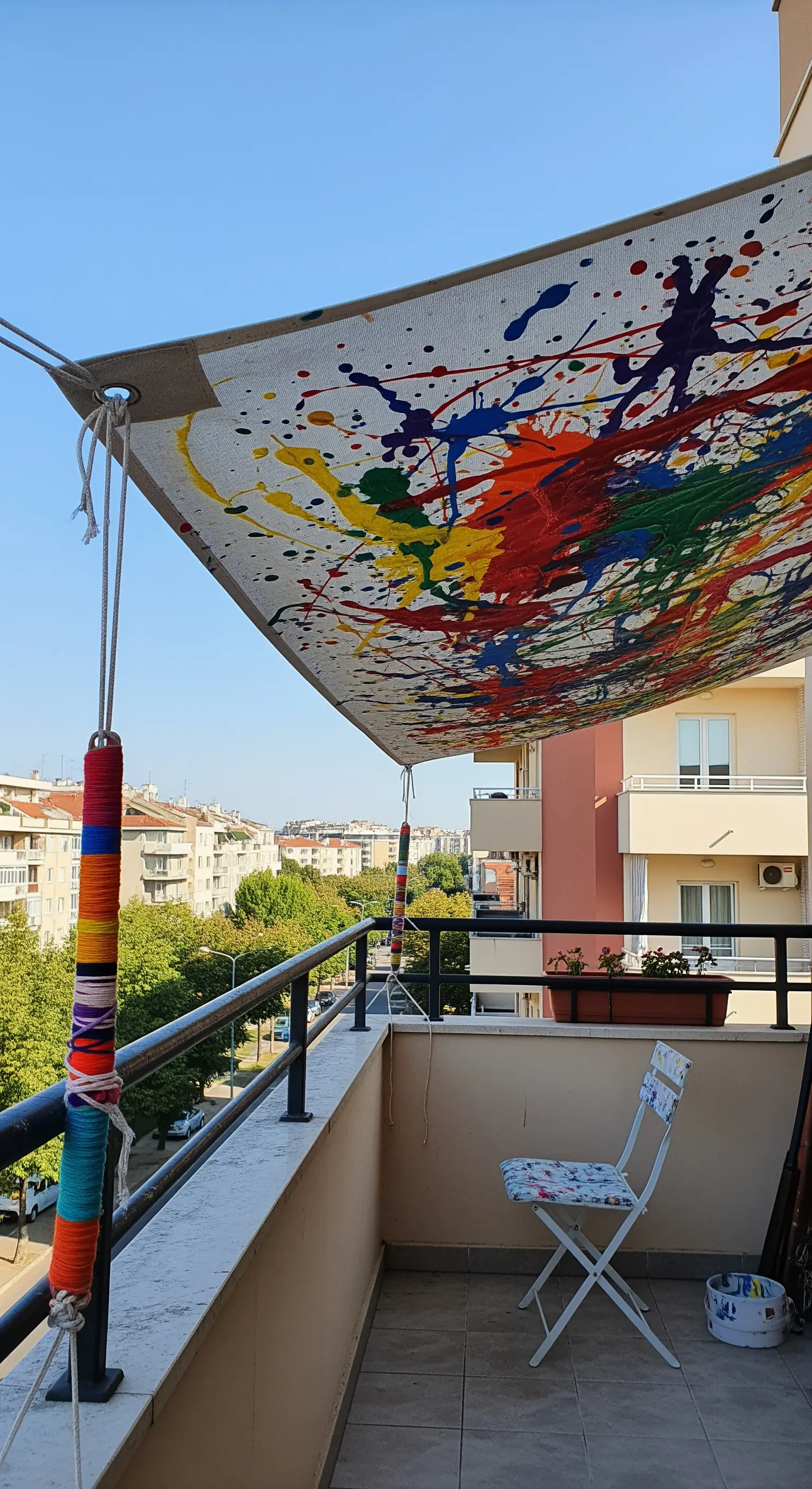 Tenda da sole su un balcone creata con una tela bianca decorata con schizzi di vernice colorata.