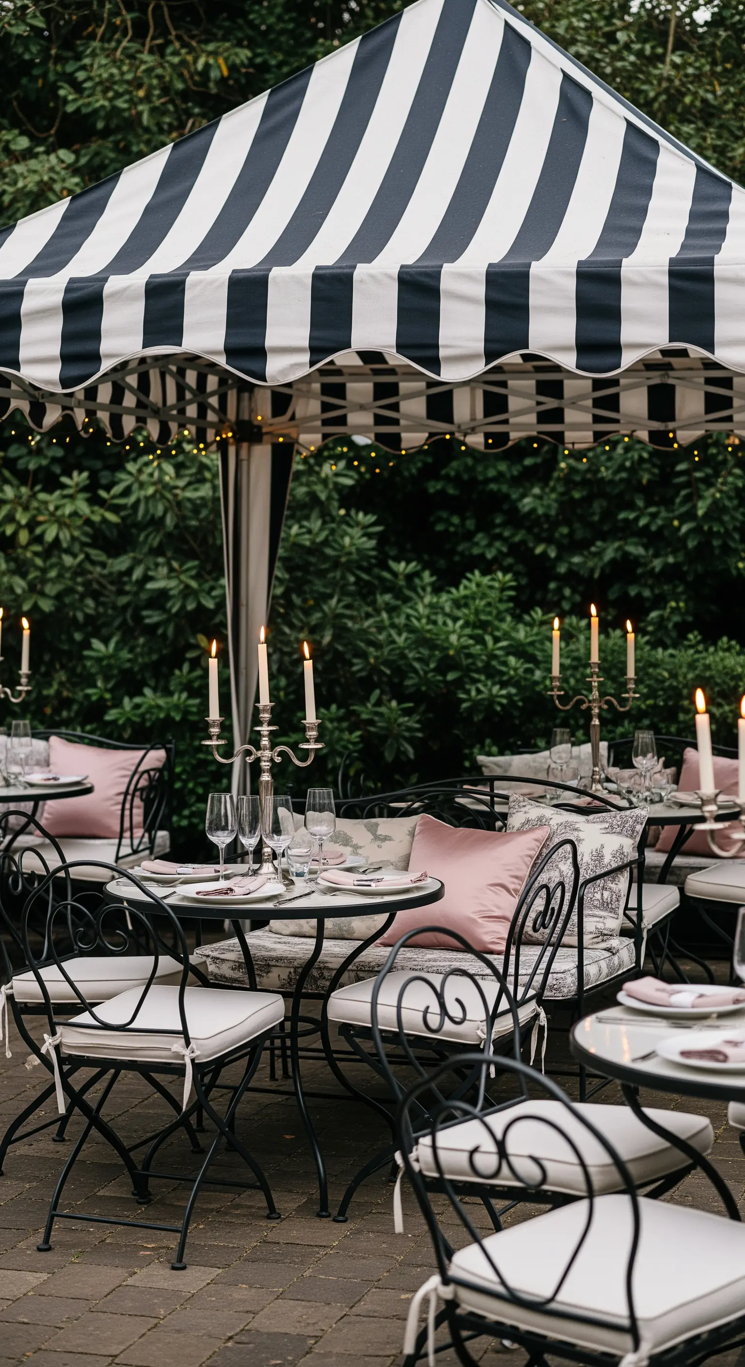 Tavoli da bistrot sotto una tenda a righe bianche e nere, con candelabri e cuscini rosa.