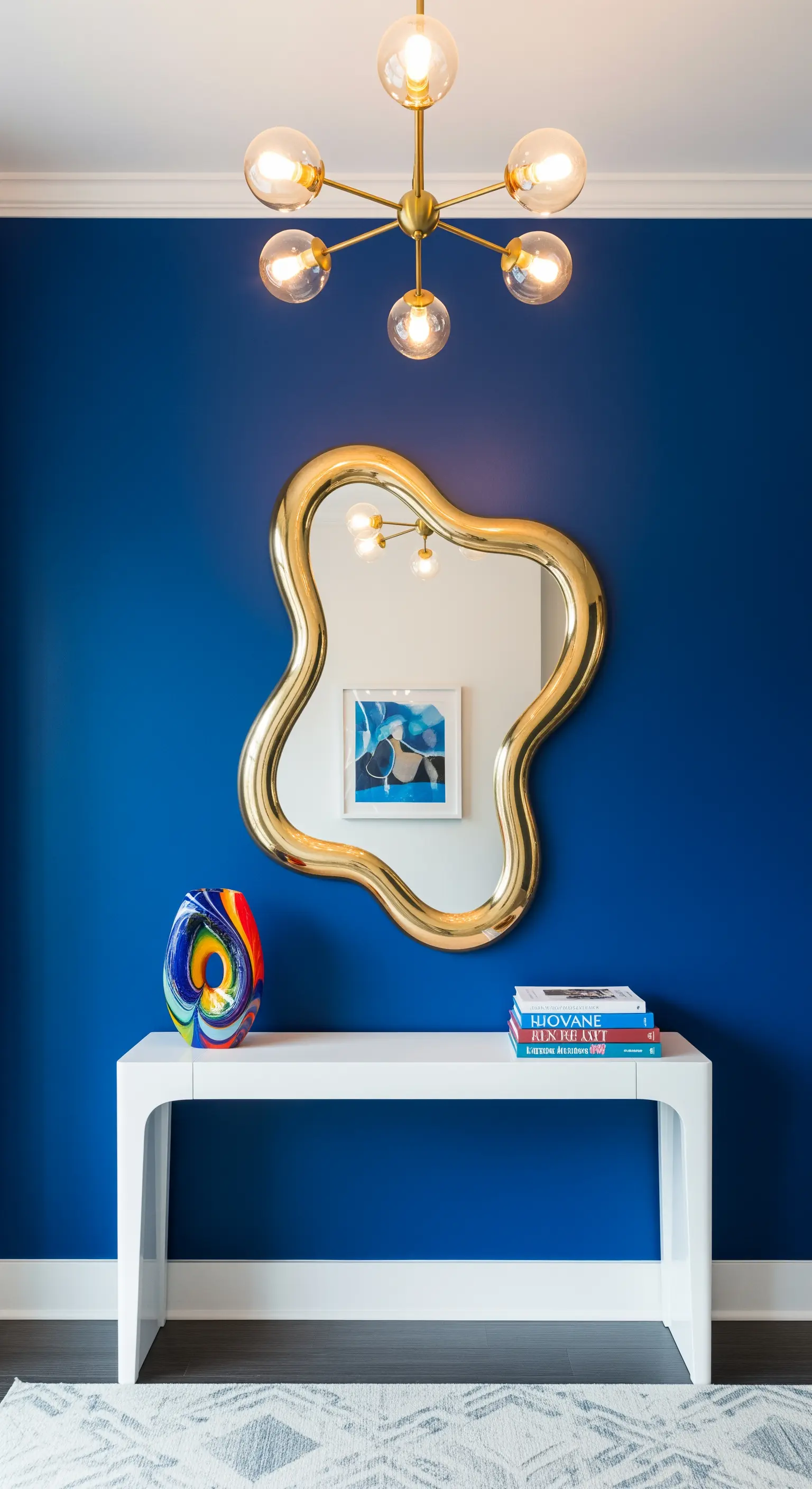 Parete blu cobalto con specchio dorato dalla forma fluida e consolle bianca minimalista.