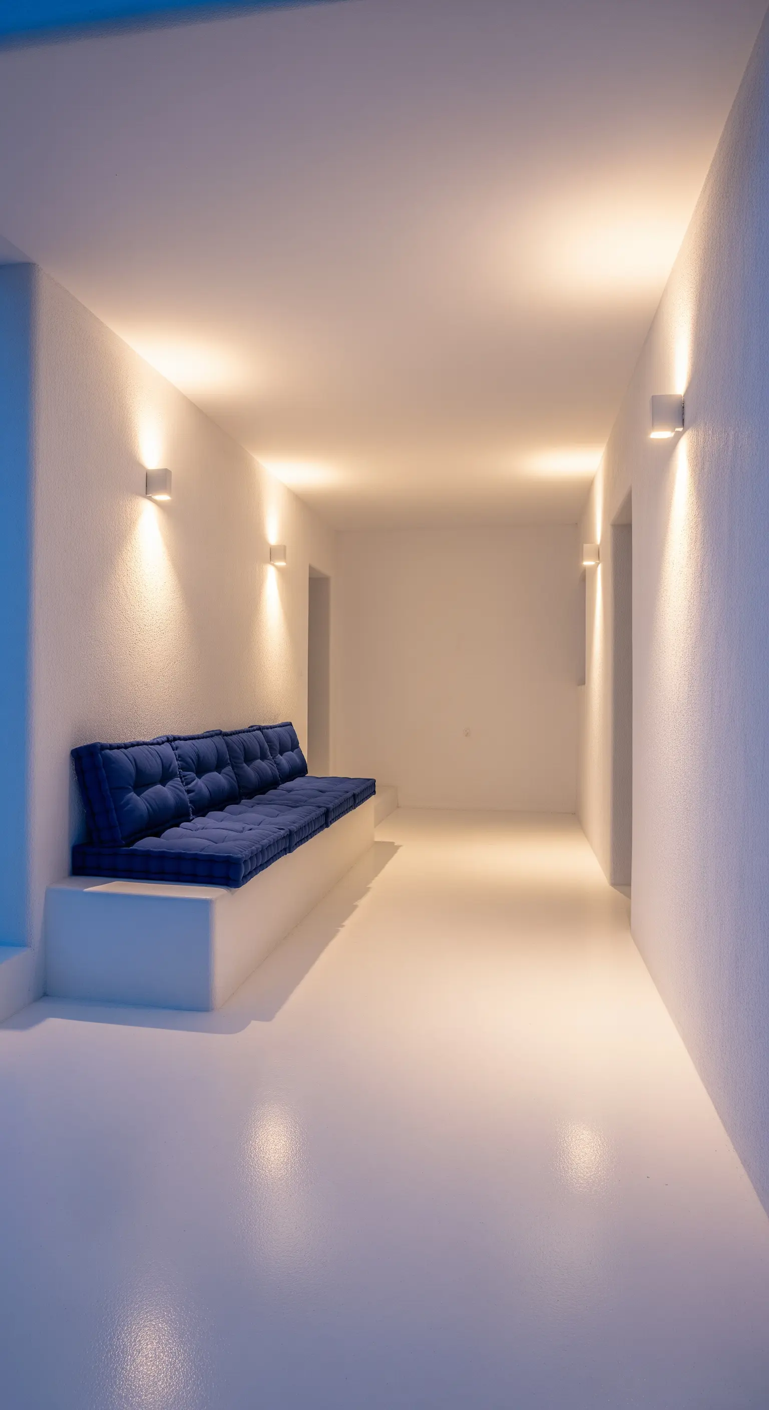 Corridoio bianco minimalista con panca in muratura e cuscini trapuntati di colore blu intenso