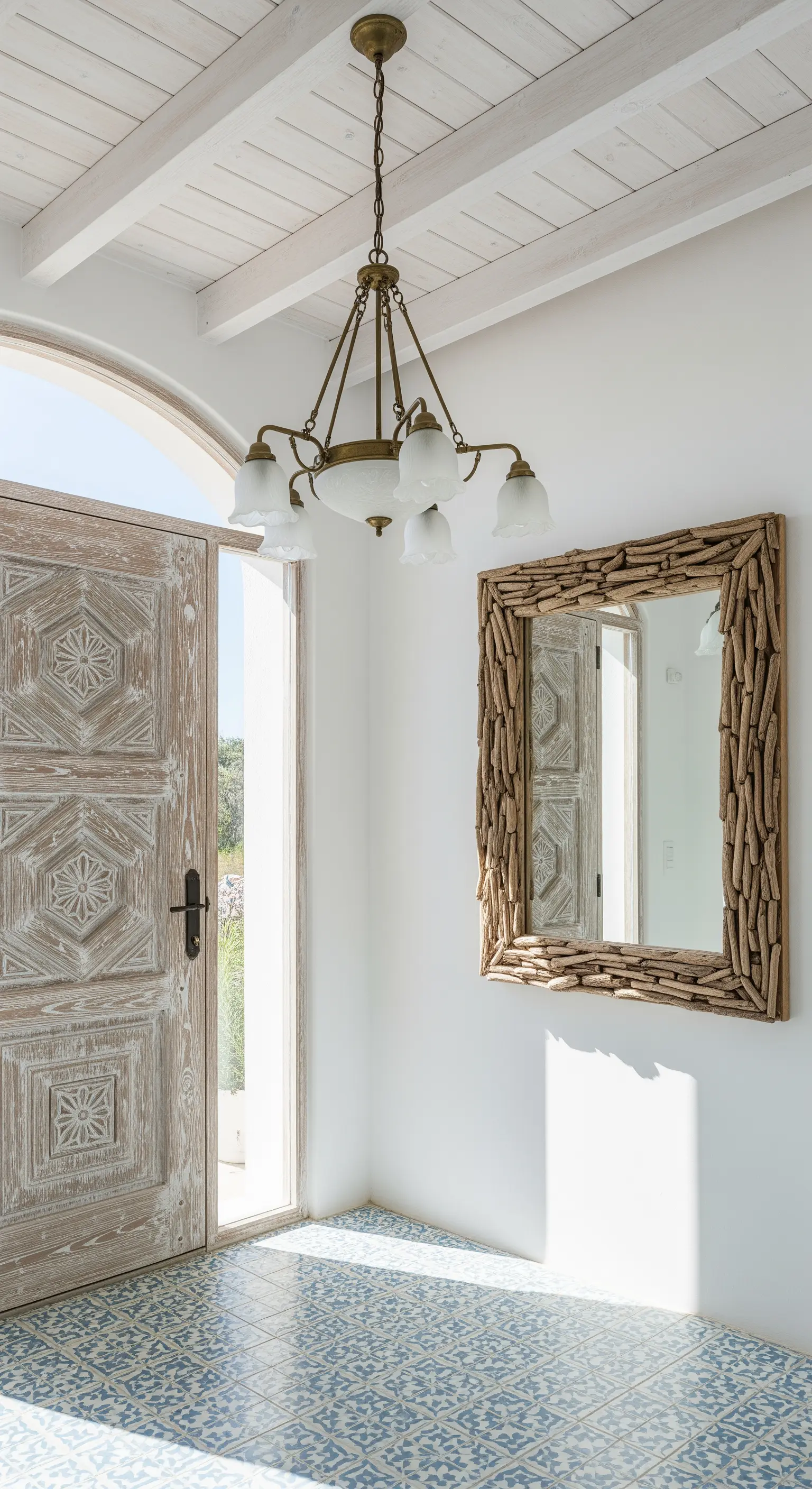 Ingresso luminoso con porta in legno sbiancato, piastrelle blu e bianche e specchio con cornice di legni.